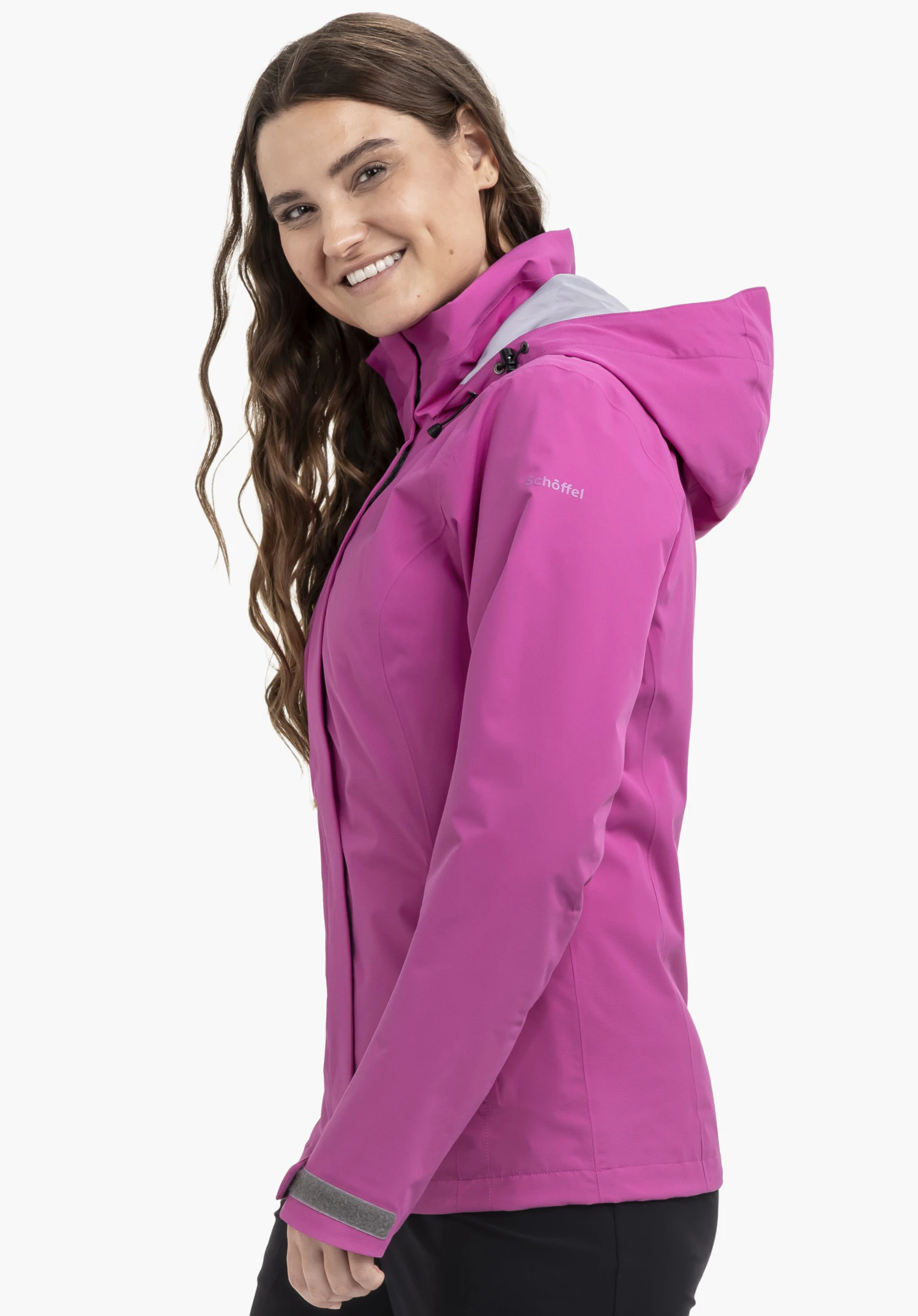 Jacket Gmund L on a model standing sideways and smiling at the camera. The pink jacket features the Schöffel logo on the sleeve and is presented against a neutral background.