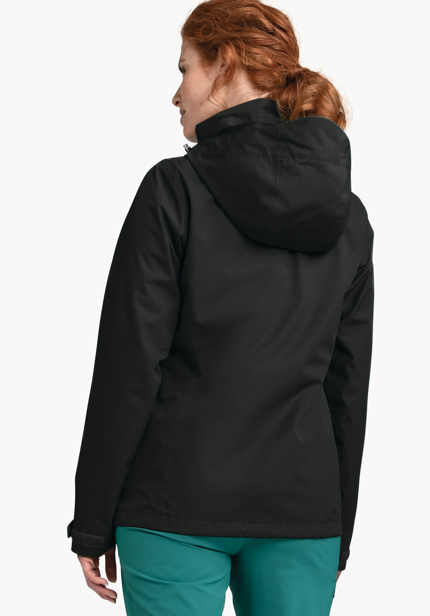 Jacket Gmund L schwarze Kapuzenjacke, von hinten getragen; Frau mit roten Haaren trägt sie und schaut seitlich; weißer Hintergrund, grüne Hose sichtbar.