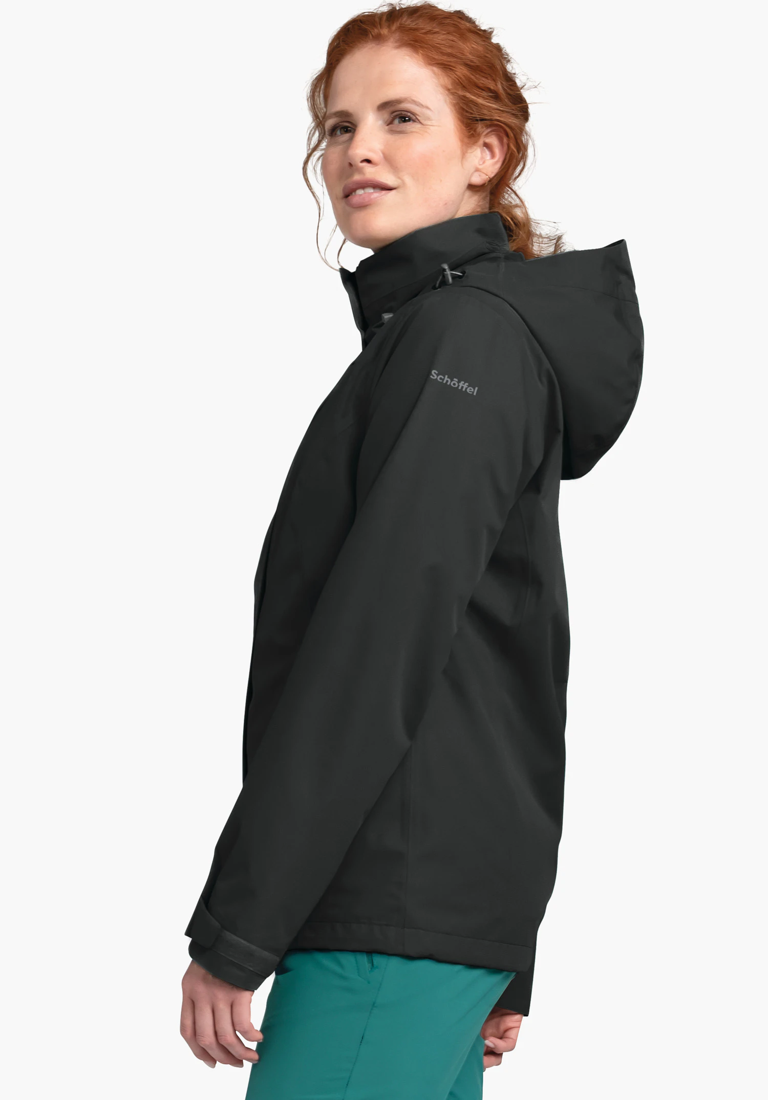 Jacket Gmund L donkergrijze regenjas, zijwaarts gedragen door een vrouw met hoog opgezette capuchon; vrouw kijkt licht omhoog. Context: lichte neutrale achtergrond. Mouwtekst: "Schöffel".