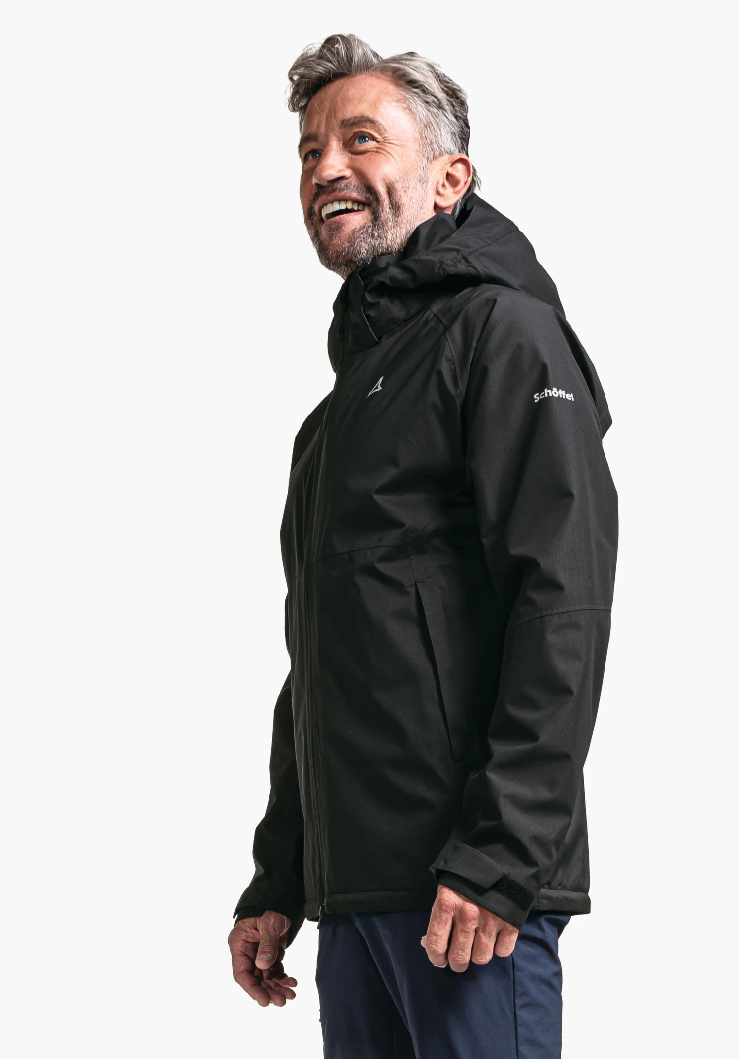 Jacket Easy XT M en noir : Un mannequin de profil devant un fond neutre présente la veste outdoor. Le logo Schöffel blanc sur la manche ainsi que la capuche sont clairement visibles.