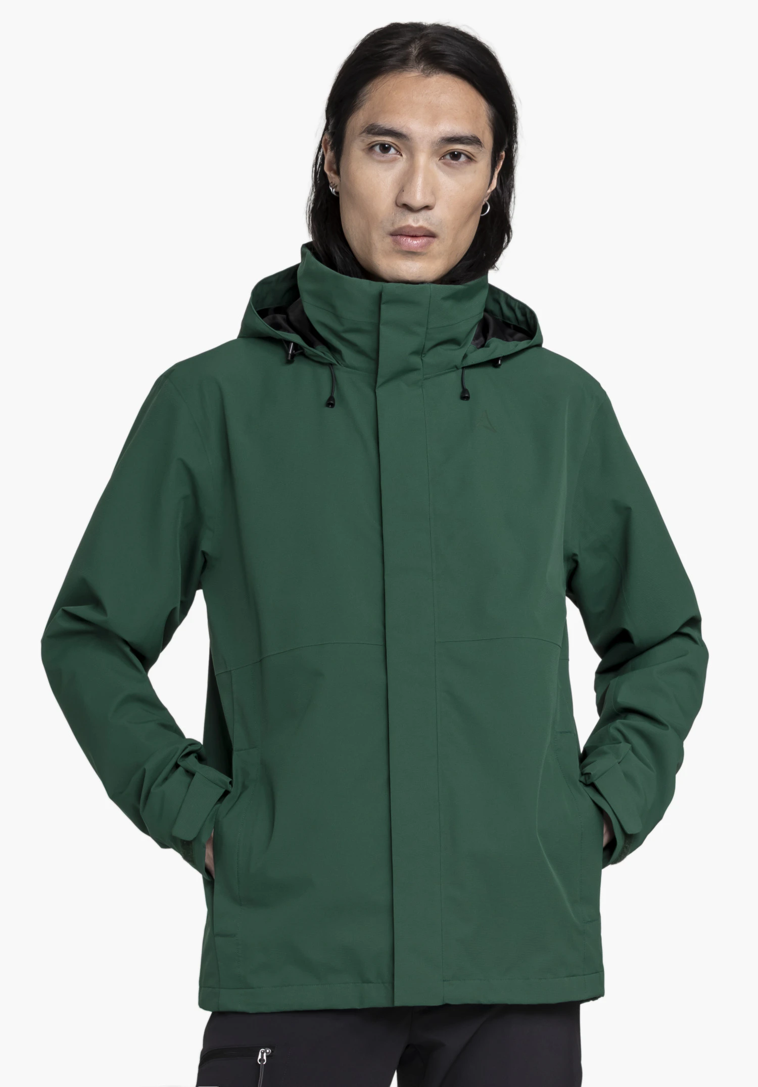 Jacket Gmund M. Un mannequin se tient de face et porte la veste verte avec les mains dans les poches, le logo Schöffel étant discrètement visible sur la poitrine gauche, présenté devant un fond neutre.