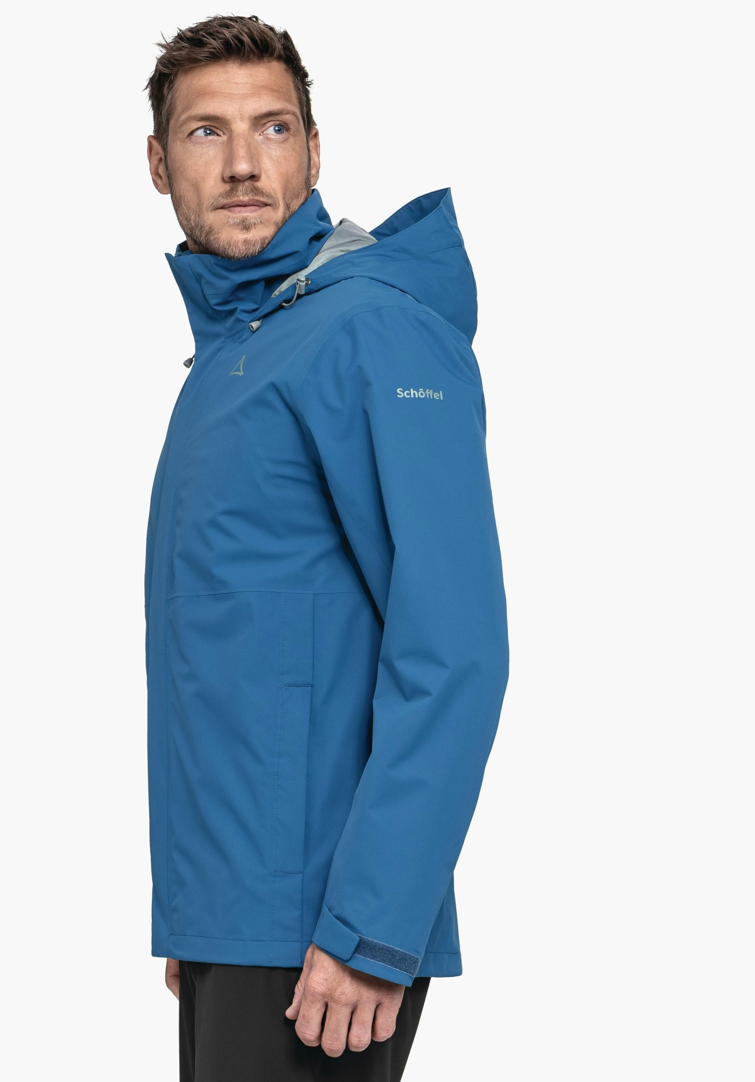 Jacket Gmund M in Blau präsentiert von einem Model, das vor einem neutralen Hintergrund seitlich in die Kamera blickt. Die Jacke zeigt sich in sportlicher Passform, während das Schöffel-Logo dezent am Oberarm platziert ist.