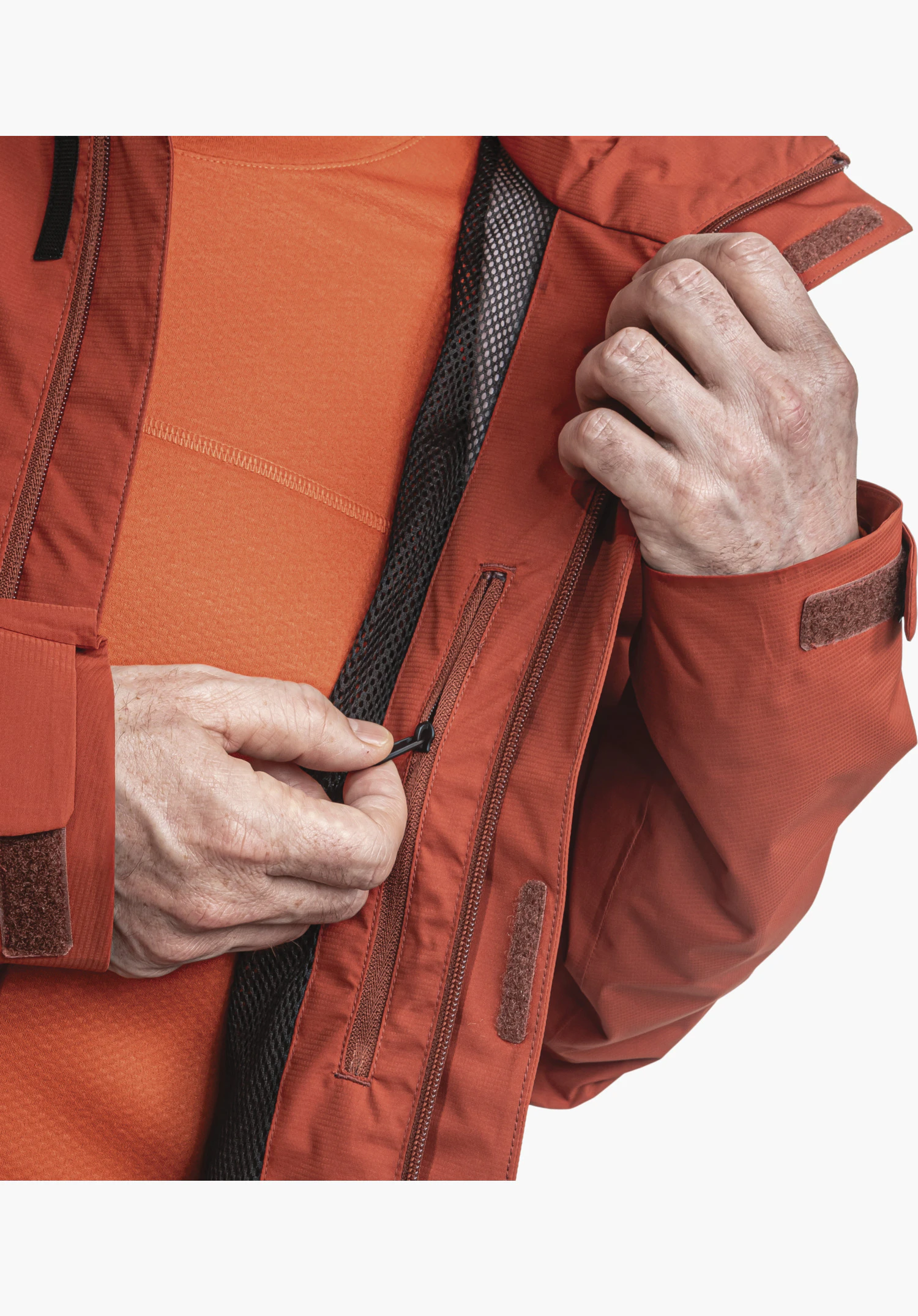 Jacket Gmund M Detail der roten Brusttasche mit Reißverschluss unter der Abdeckleiste. Eine Hand greift den Zipper und enthüllt das schwarze Mesh-Futter, Nahaufnahme vor weißem/neutralem Hintergrund.