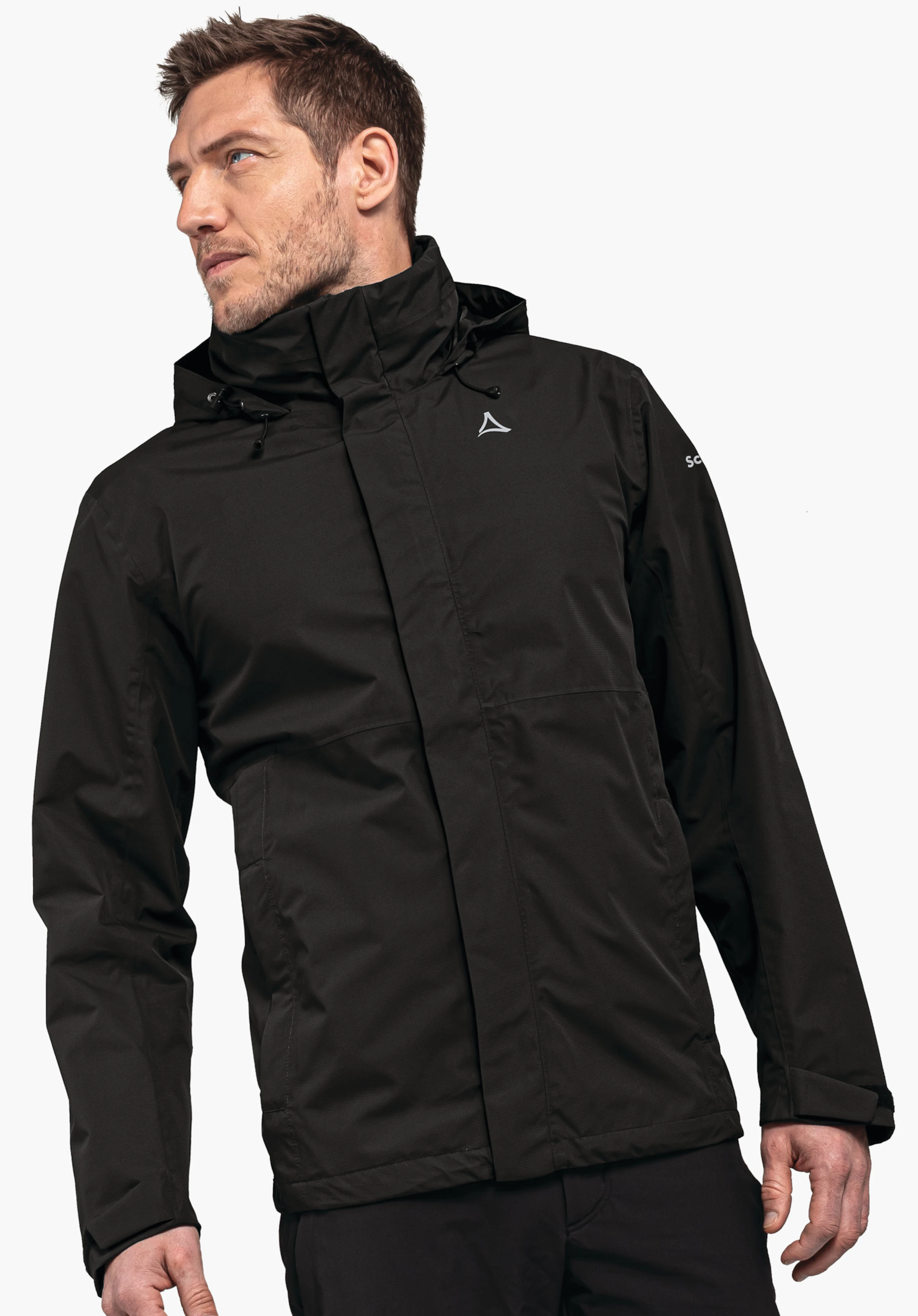 Jacket Gmund M Veste de pluie noire avec logo Schöffel blanc, portée par un homme regardant légèrement vers la gauche; capuche relevée; fond clair uni. Texte sur la manche: « SC ».