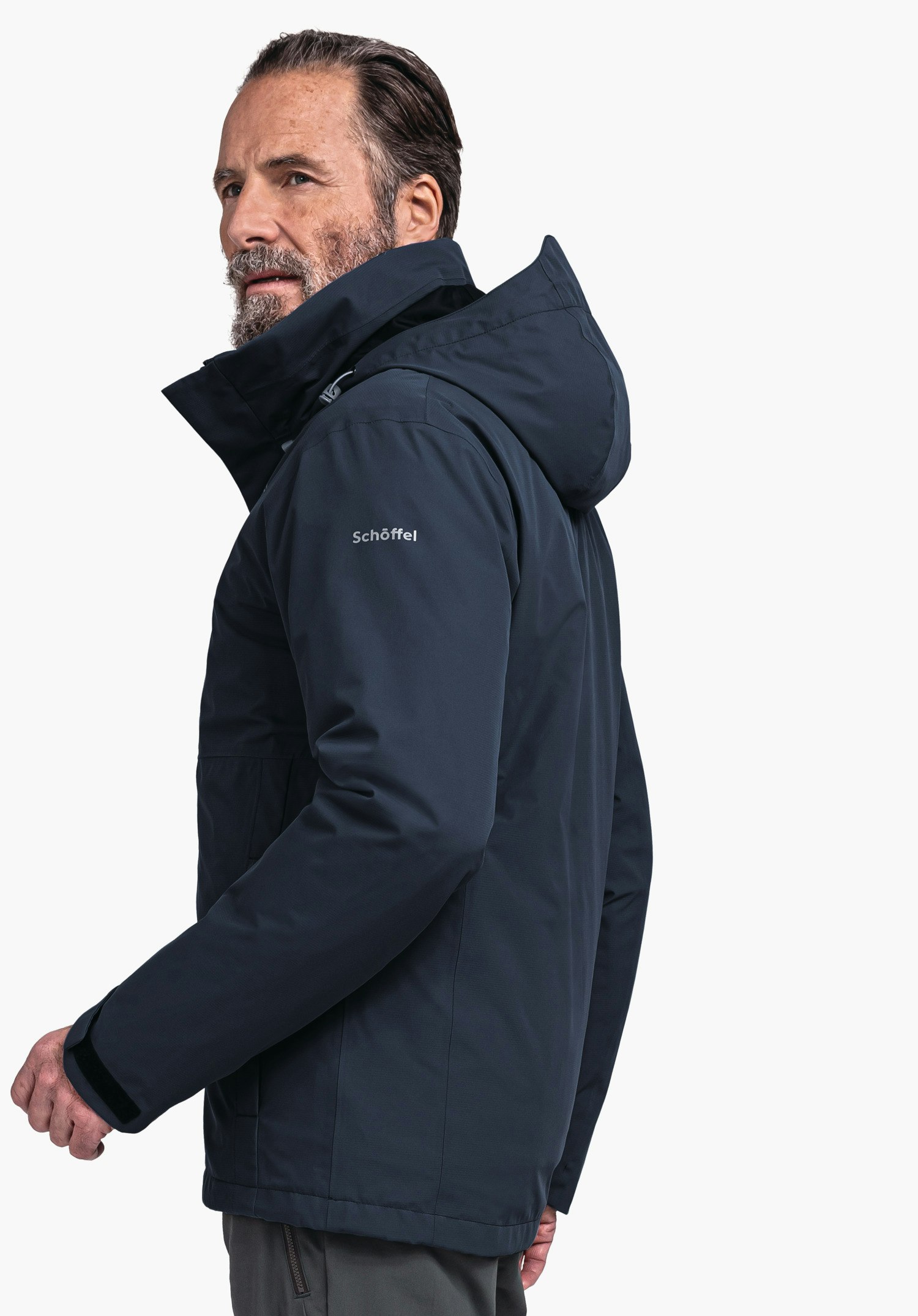 Jacket Gmund M Dunkelblaue Jacke, Mann trägt sie und blickt seitlich über die Schulter; Kapuze hochgeklappt; auf dem Ärmel Text "Schöffel"; neutraler weißer Hintergrund.