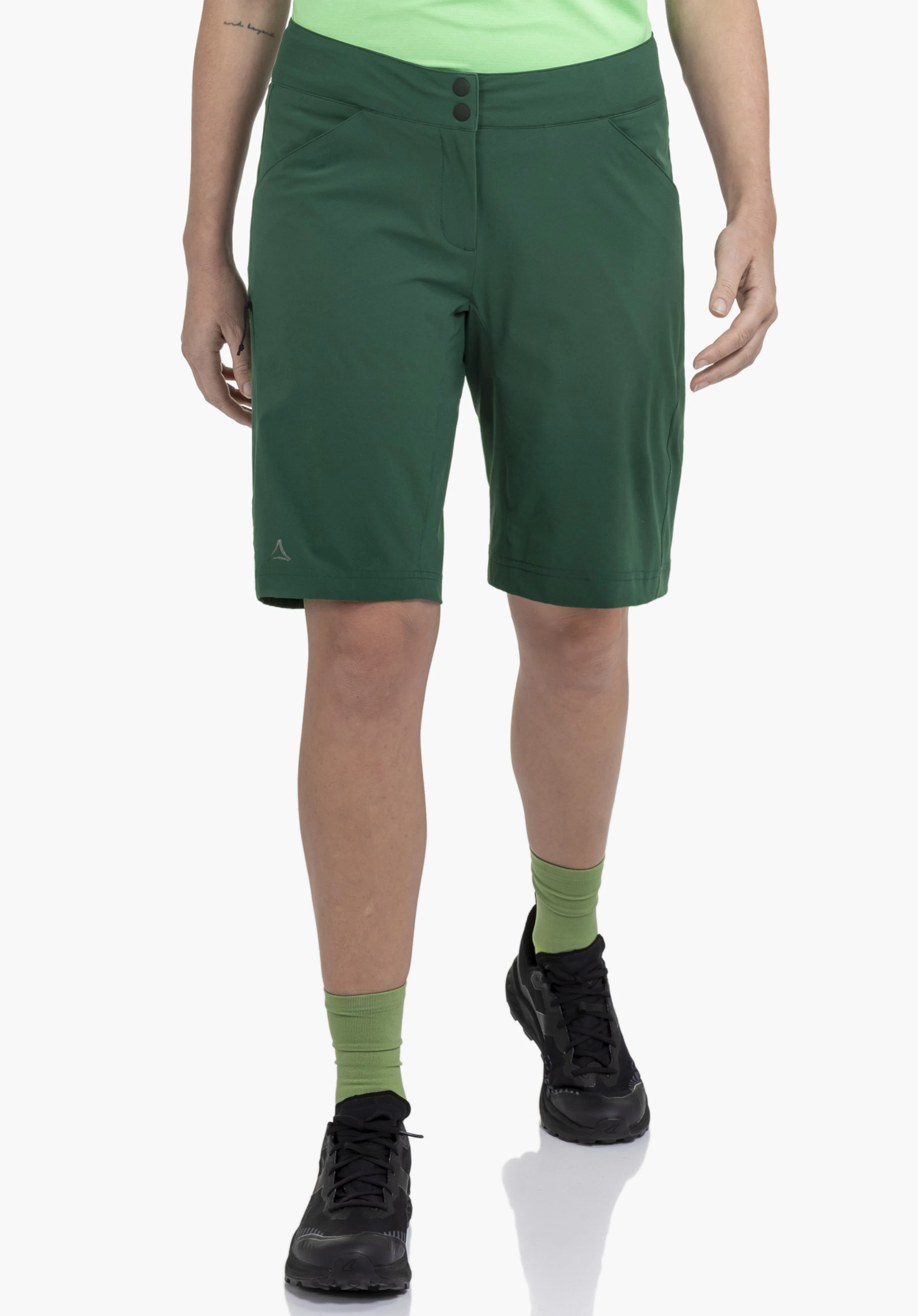 Shorts Danube L porté par un mannequin de face faisant un léger pas en avant. Le short vert présente le logo Schöffel sur le bas de la jambe droite, photographié sur un fond neutre.