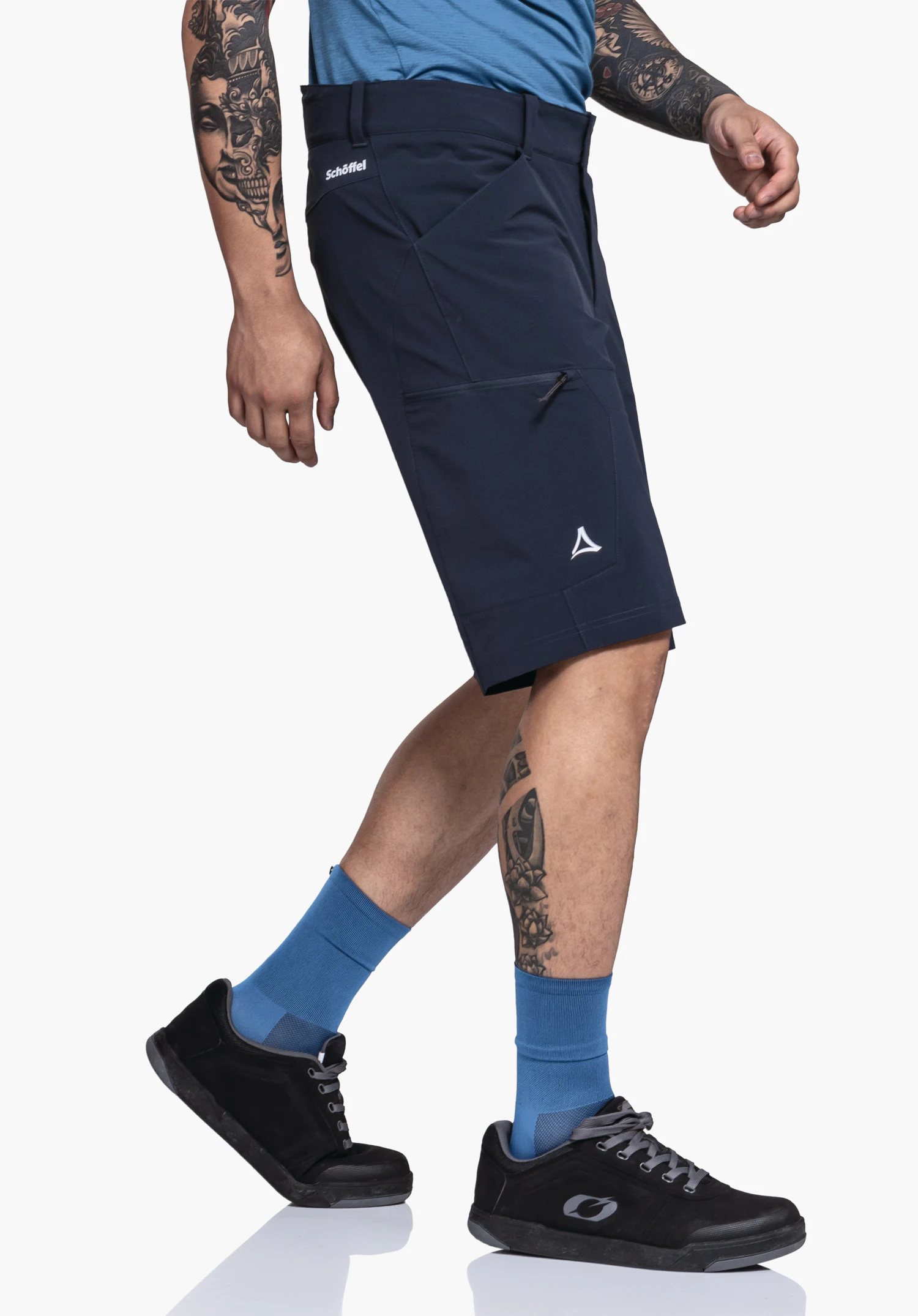 Shorts Danube M in blauw. Een model staat zijwaarts voor een neutrale achtergrond en presenteert de shorts tijdens een actieve stap. Het subtiele Schöffel-logo is zichtbaar onder de zak op het been.