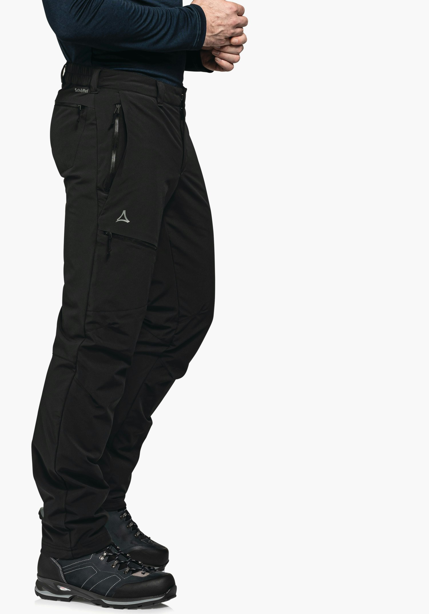 Pants Koper1 Warm M schwarze Outdoorhose, steht seitlich, Beine leicht gebeugt; Person mit gefalteten Händen, trägt dunkelblaues Oberteil; Studiohintergrund weiß. Schöffel-Logo sichtbar; Text: "Schöffel".