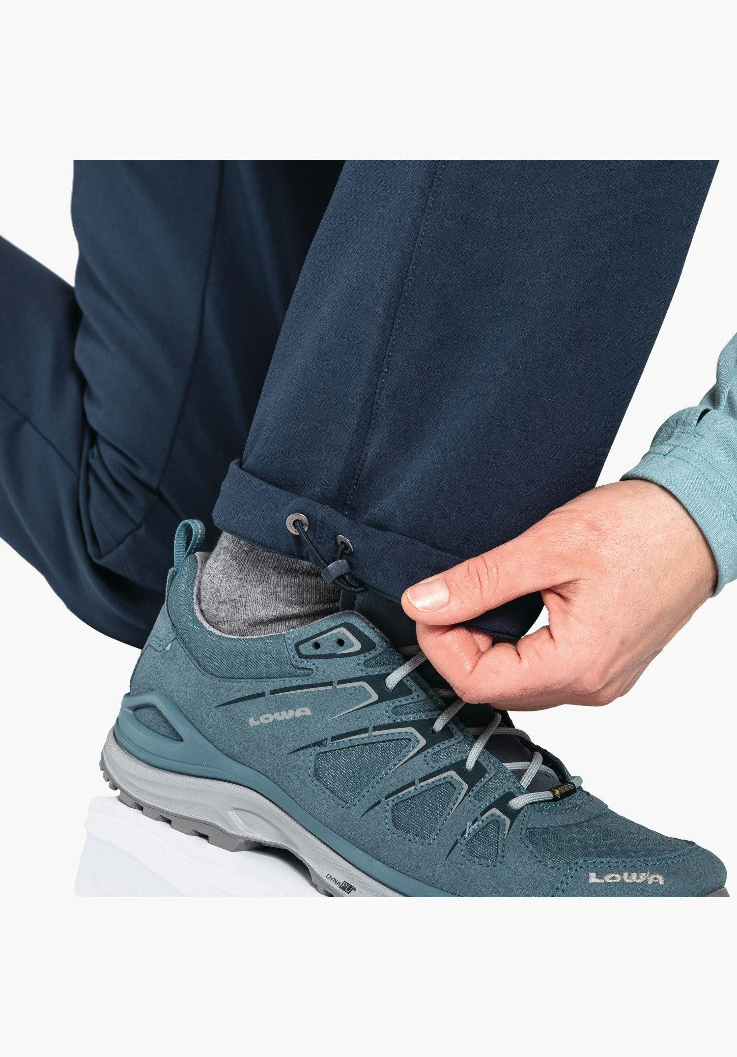 Pants Ascona Warm L zeigt den verstellbaren Beinsaum mit Kordelzug in Blau, wobei eine Hand gerade die Weite am Stopper reguliert. Nahaufnahme vor weißem/neutralem Hintergrund.