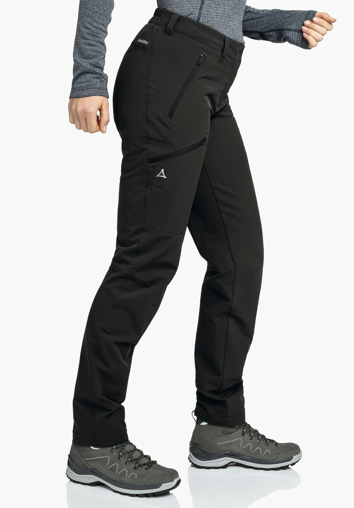 Pants Ascona Warm L black outdoor trousers worn side-on, stepping forward; person wears a dark grey top and dark grey hiking shoes on a white background. Text: "Schöffel". Schöffel logo visible.