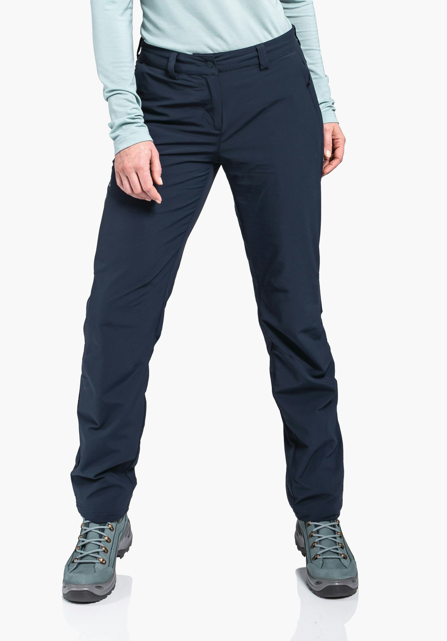 Pants Engadin1 Warm L Pantalon femme bleu foncé, debout jambes légèrement écartées et mains le long du corps; contexte: fond clair, haut bleu clair, chaussures de randonnée vert clair.