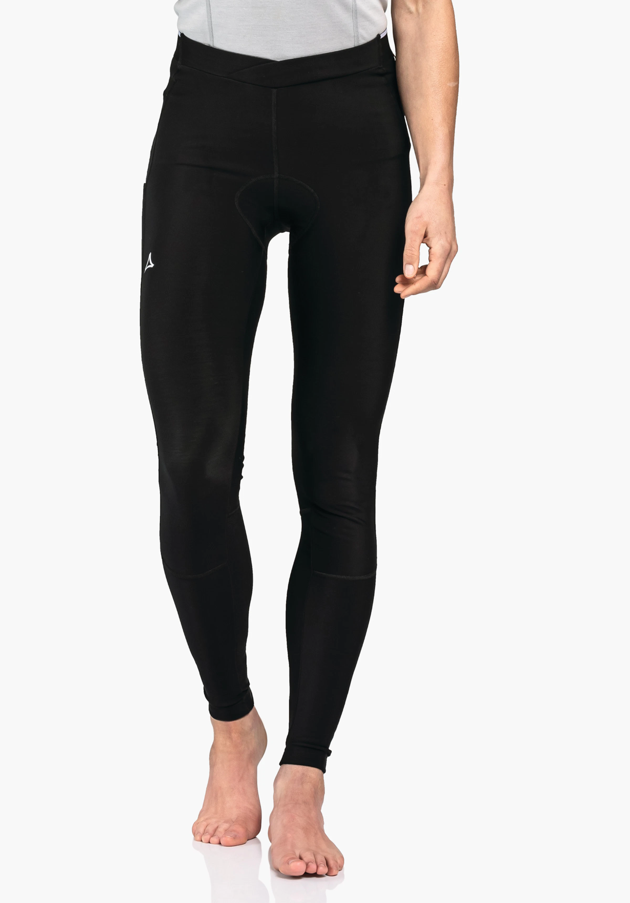 Skin Pants Warm 4h L leggings de sport noirs ajustés avec logo Schöffel sur la cuisse gauche; portés par une personne debout pieds nus; fond studio blanc.