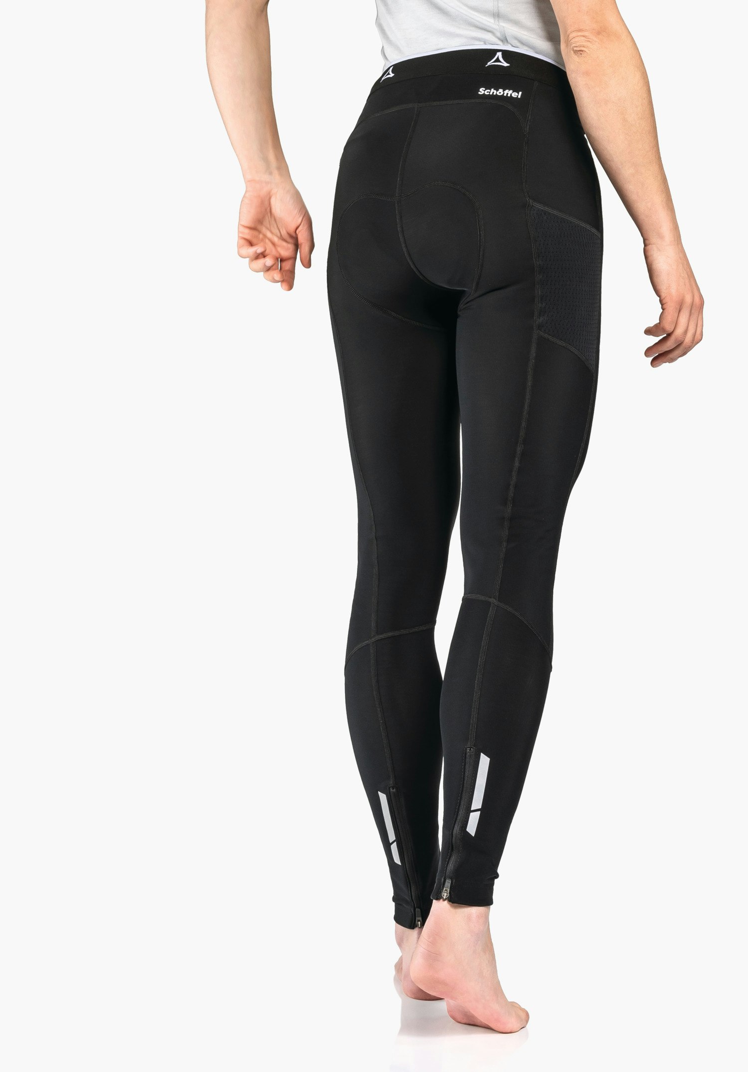 Skin Pants Warm 4h L leggings noirs portés près du corps, vue arrière; jambes légèrement en arrière, pieds nus sur fond clair. Logo Schöffel et inscription « Schöffel » visibles.