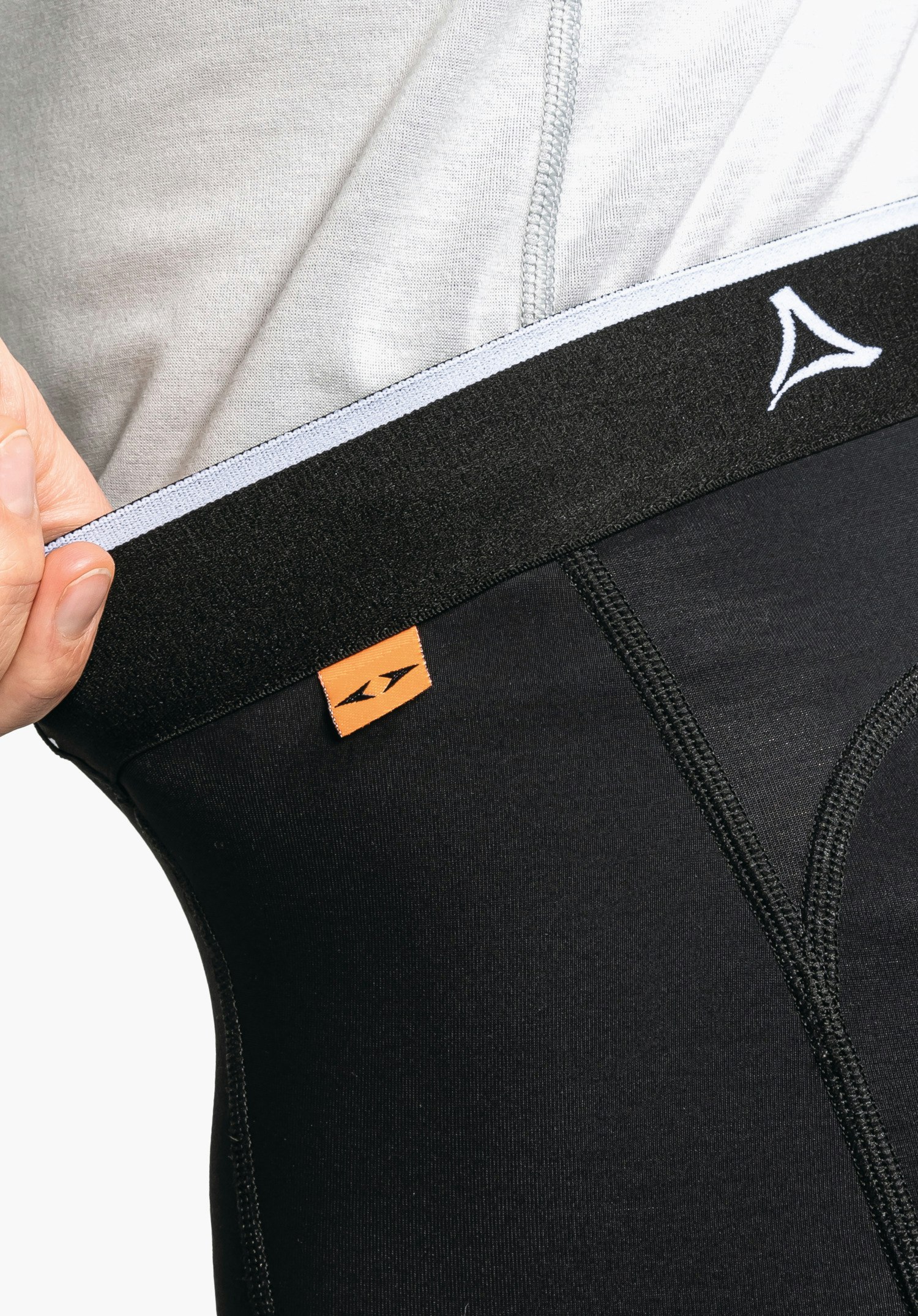 Skin Pants Warm 4h L. La ceinture élastique noire avec le logo Schöffel blanc et une petite étiquette tissée orange. Gros plan sur fond blanc/neutre.