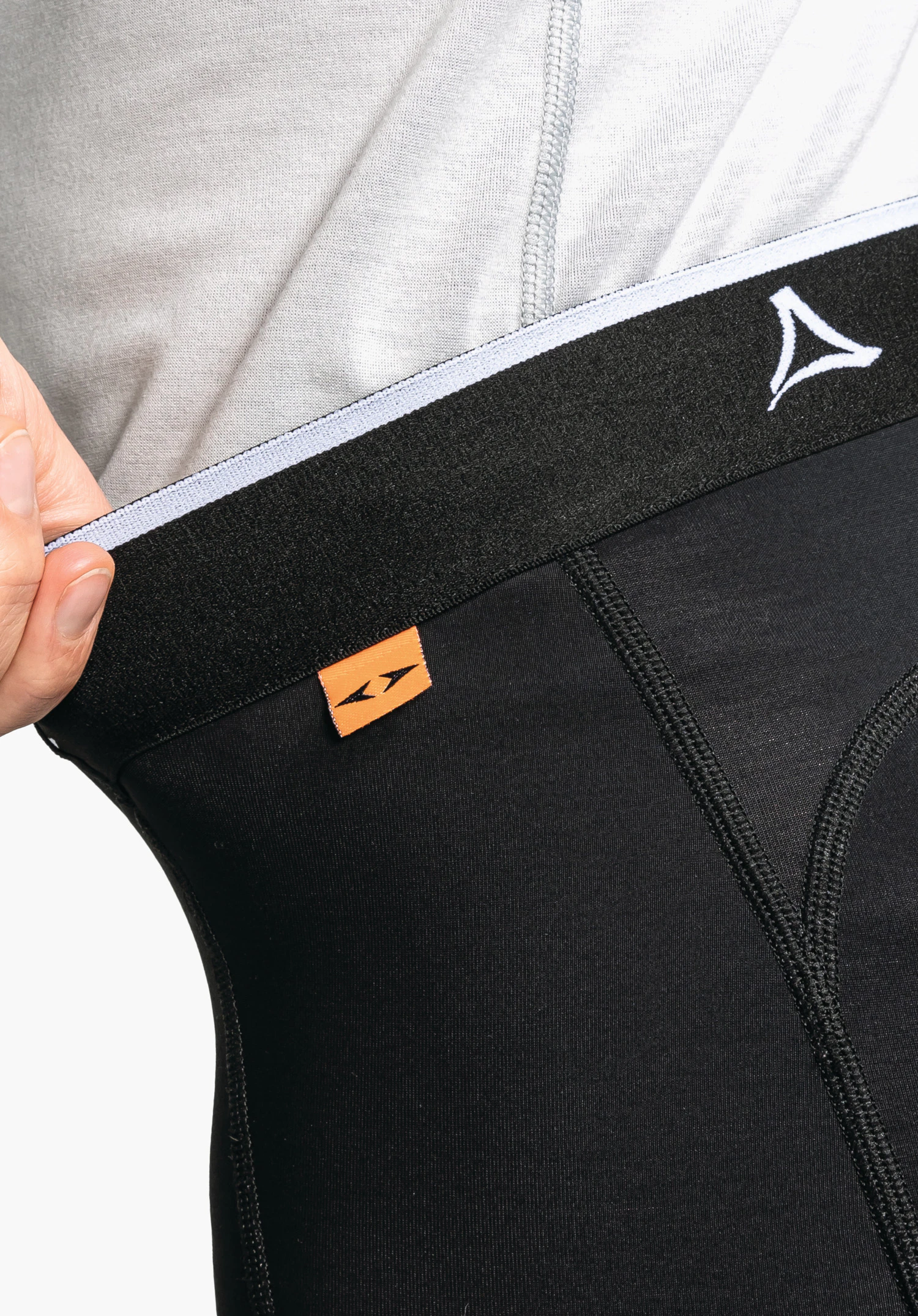 Skin Pants Warm 4h L. La ceinture élastique noire avec le logo Schöffel blanc et une petite étiquette tissée orange. Gros plan sur fond blanc/neutre.