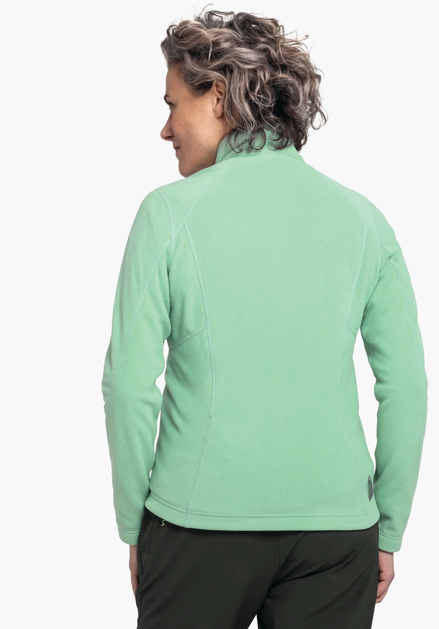 Fleece Jacket Leona3 veste polaire vert clair, portée par une personne debout dos à la caméra, veste fermée, bras détendus sur les côtés; fond blanc; petit logo Schöffel sous forme d’étiquette au bas droit.
