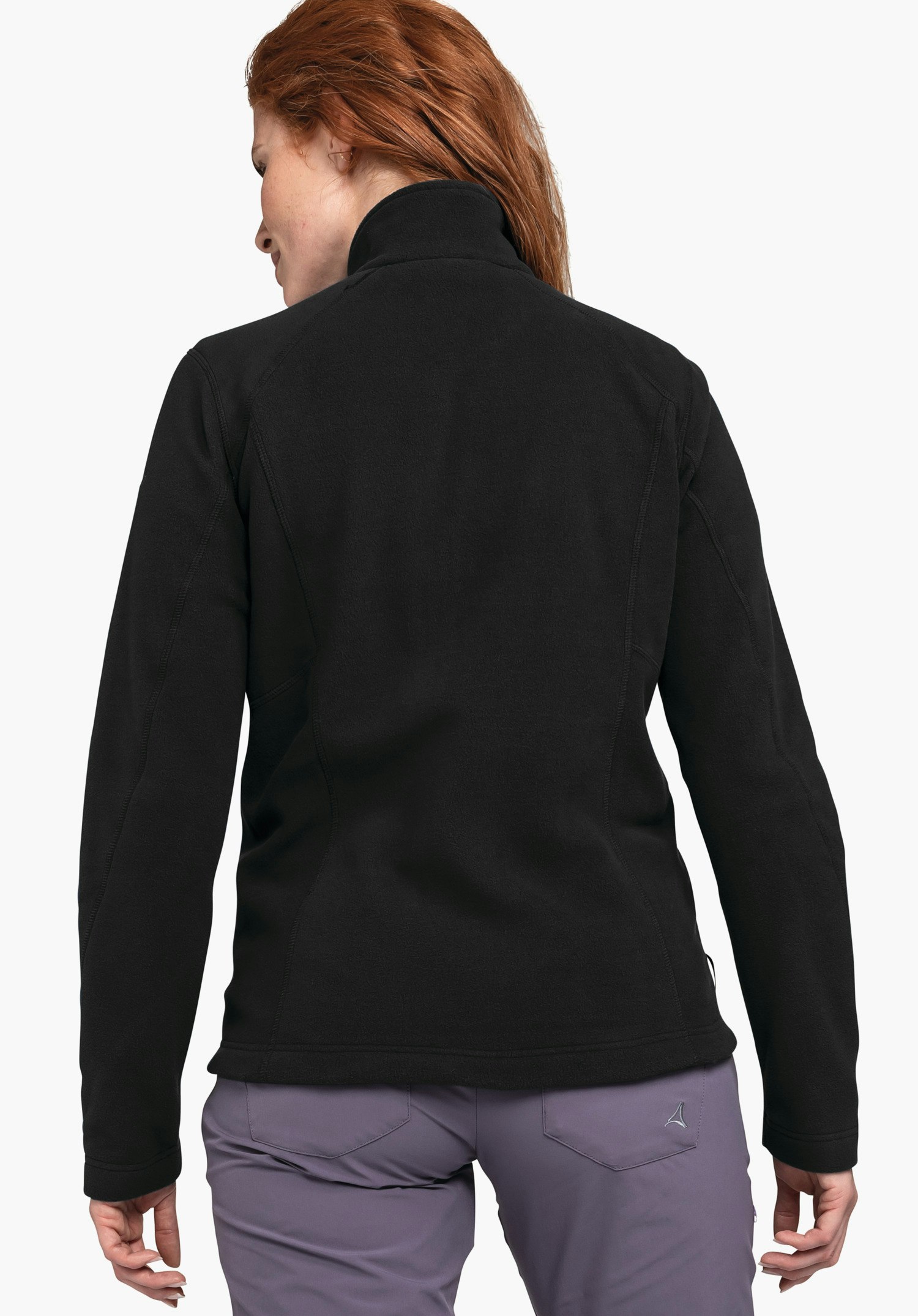 Fleece Jacket Leona3 veste noire, portée de dos; fond clair neutre; pantalon violet clair avec logo Schöffel visible sur la poche arrière droite; cheveux rouge foncé.