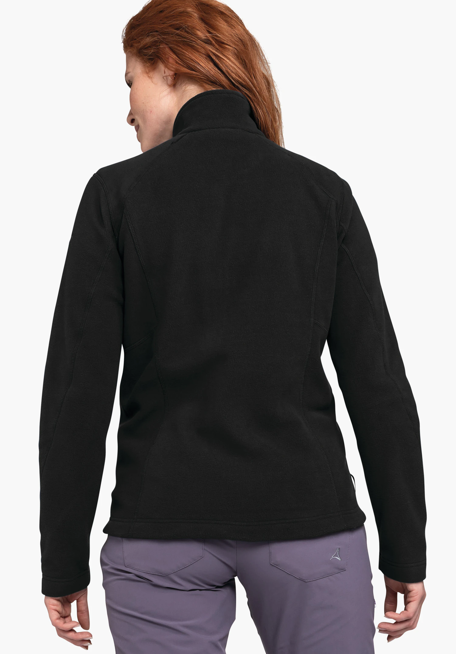 Fleece Jacket Leona3 black jacket worn from the back; neutral light background; person wears light purple trousers with visible Schöffel logo on the right back pocket; dark red hair.