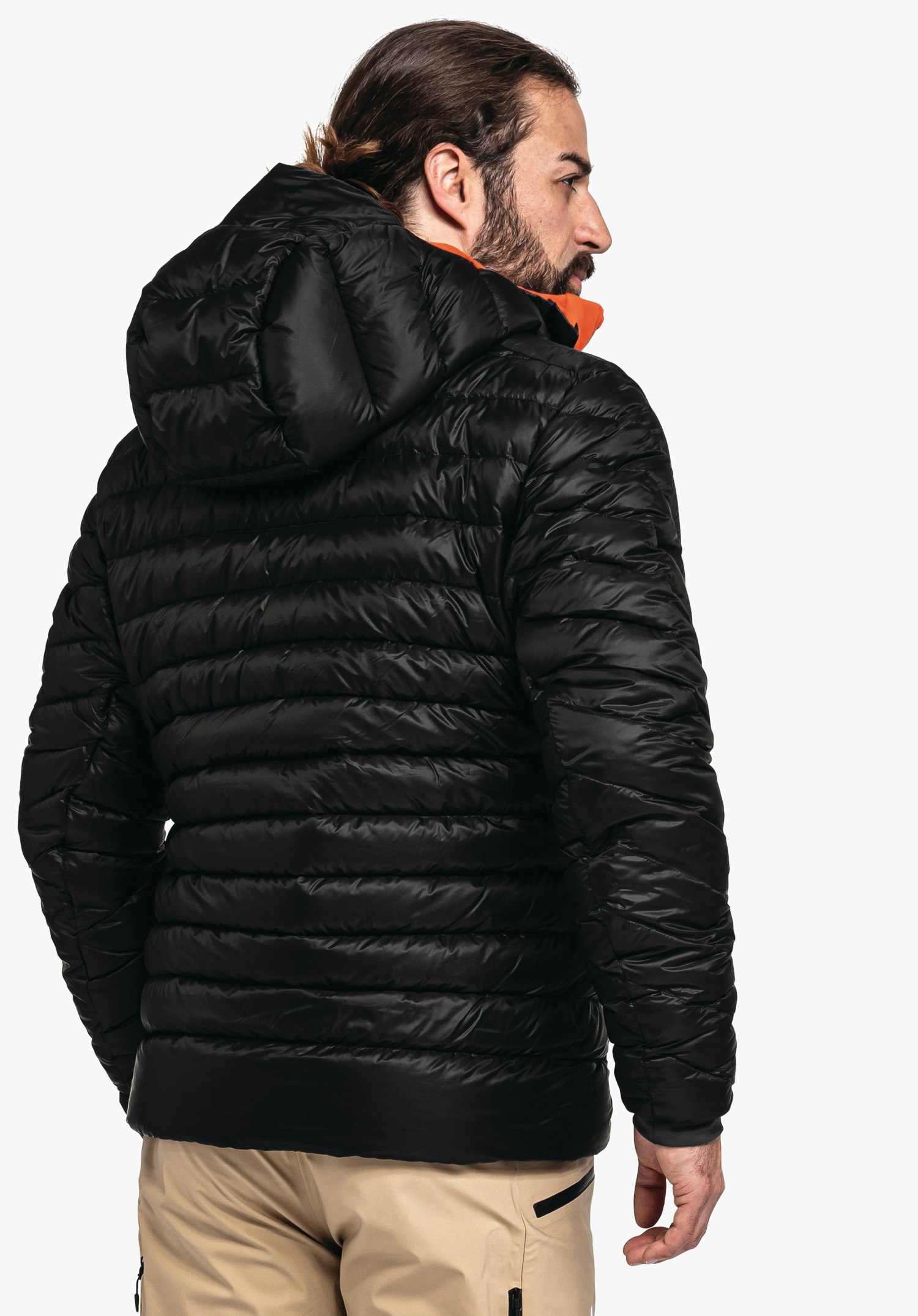 Down Jacket Silvretta M dunkelschwarze Steppjacke, getragen von einem Mann, der sich nach rechts dreht; sichtbare Kapuze und gestepptes Muster, weißer Studiohintergrund.