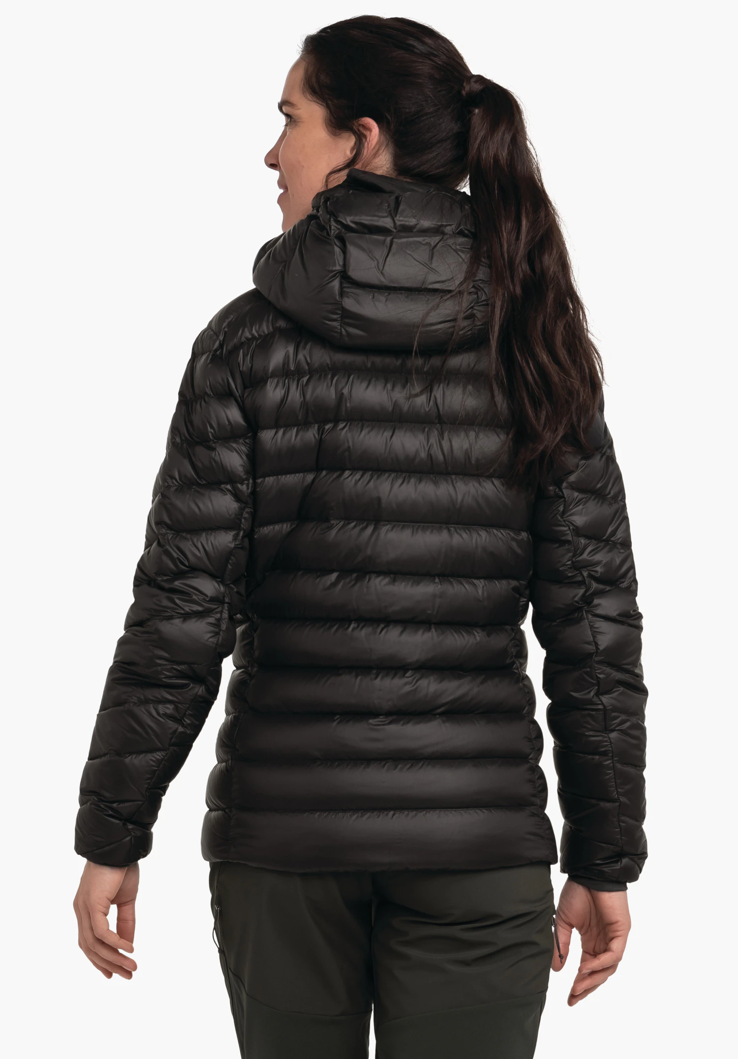 Down Jacket Silvretta L schwarze Daunenjacke von hinten getragen, stehende Person; Kapuze und horizontale Steppungen; Kontext: weißer Studiohintergrund, dunkelgrüne Hosen.
