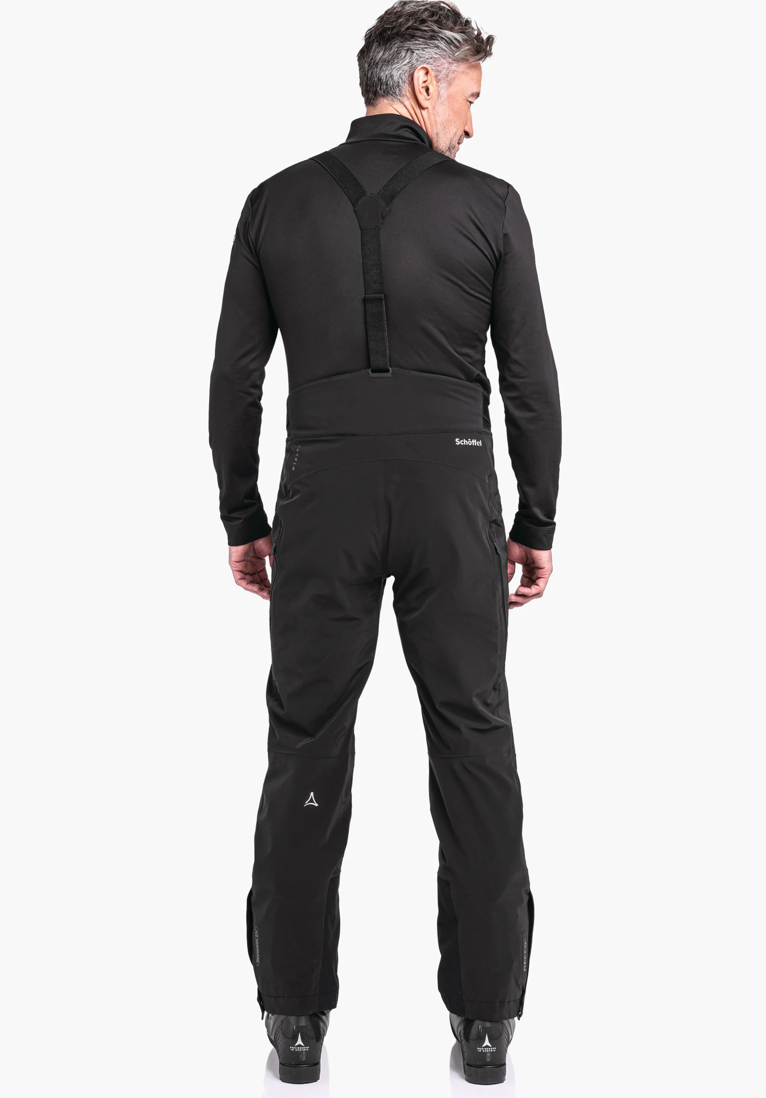 Ski Pants Trevalli M black softshell ski trousers with braces worn by a man; stands with back to the viewer and looks to the right; bright studio setting; “Schöffel” lettering and Schöffel logo visible.