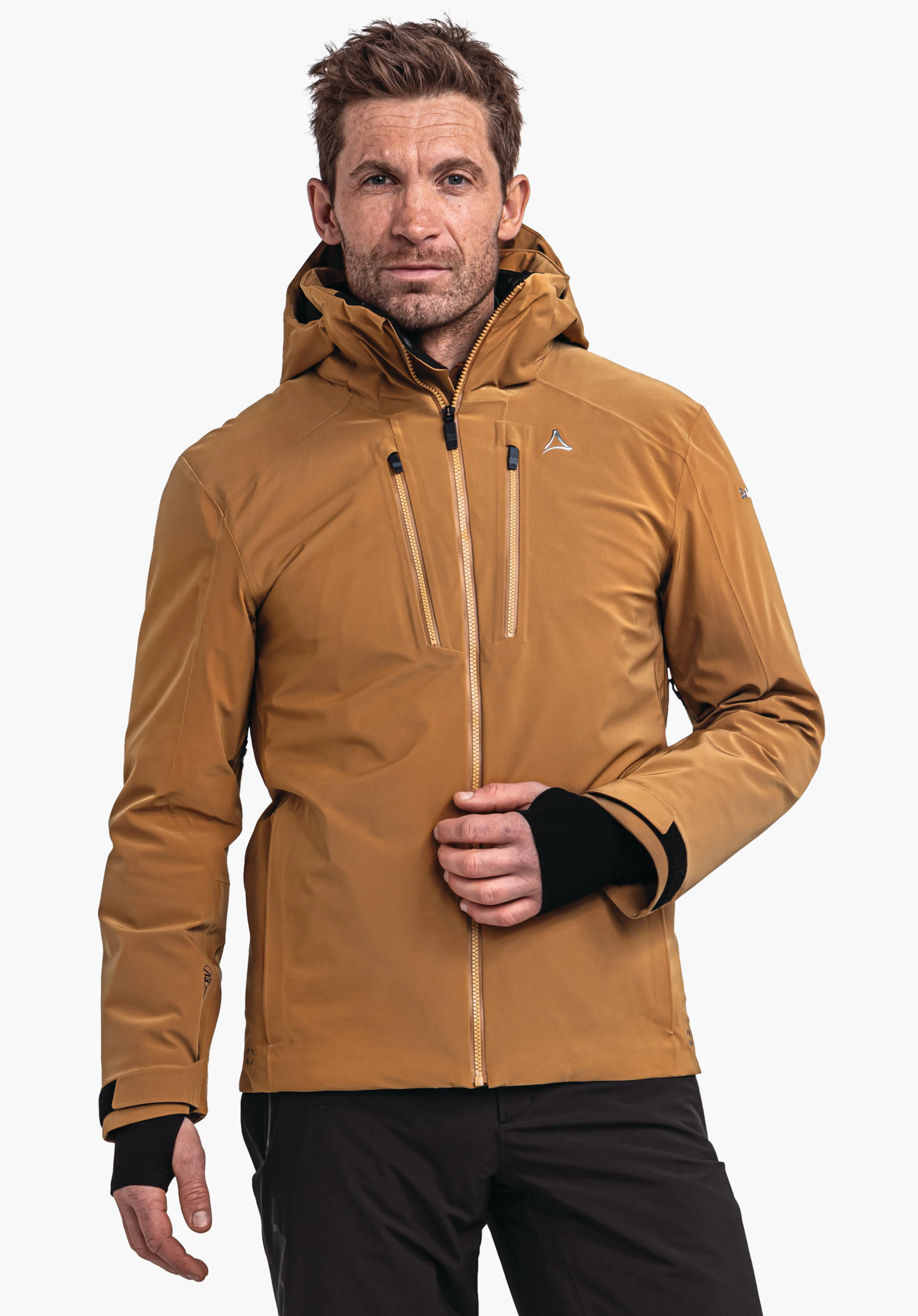 Ski Jacket Verbier M donkeroranje jas met capuchon en Schöffel-logo; man houdt de voorste ritssluiting vast met de rechterhand; zwarte mouwboorden zichtbaar, zwarte broek, witte achtergrond.