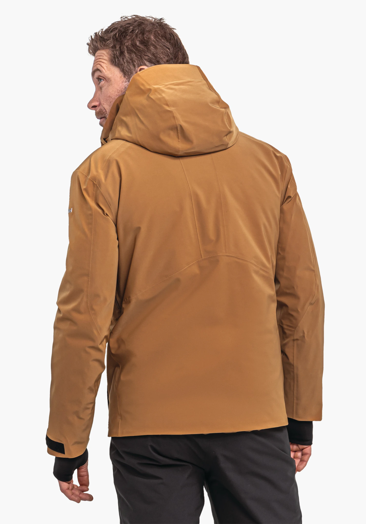 Ski Jacket Verbier M donkeroranje jas met capuchon, gedragen door een man van achteren; hij kijkt opzij, jas valt los, handen ontspannen, witte achtergrond, zwarte broek.