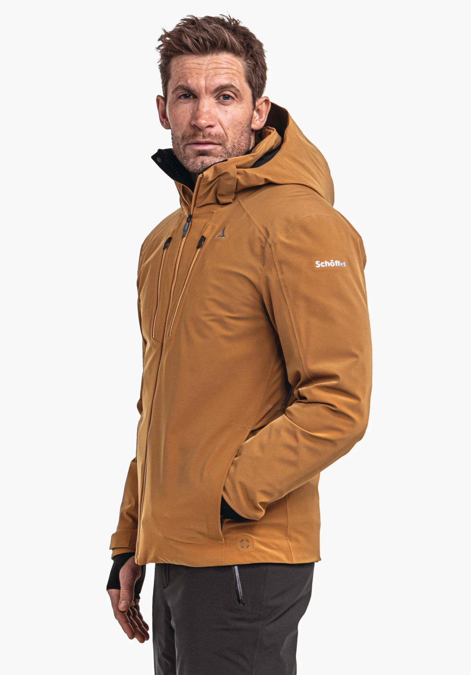 Ski Jacket Verbier M donkeroranje jas, gedragen door een man met opgezette capuchon en handen in de zakken, voor een lichte achtergrond; Schöffel-logo zichtbaar op de borst, tekst "Schöffel" op de mouw.
