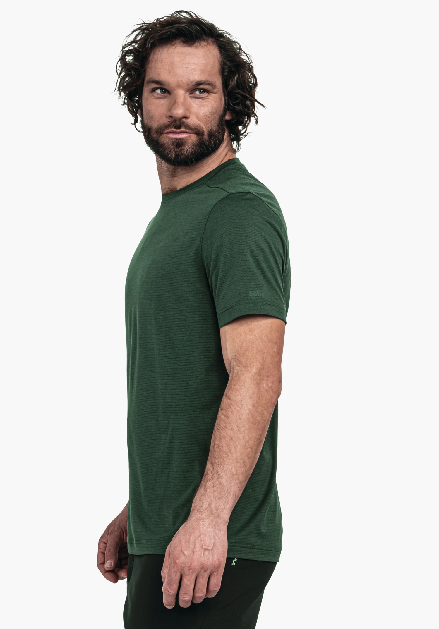 CIRC T Shirt Tauron M t-shirt porté par un modèle masculin; t-shirt vert foncé, position latérale, regard vers la gauche; bras détendus, barbe et cheveux ondulés, fond blanc neutre.