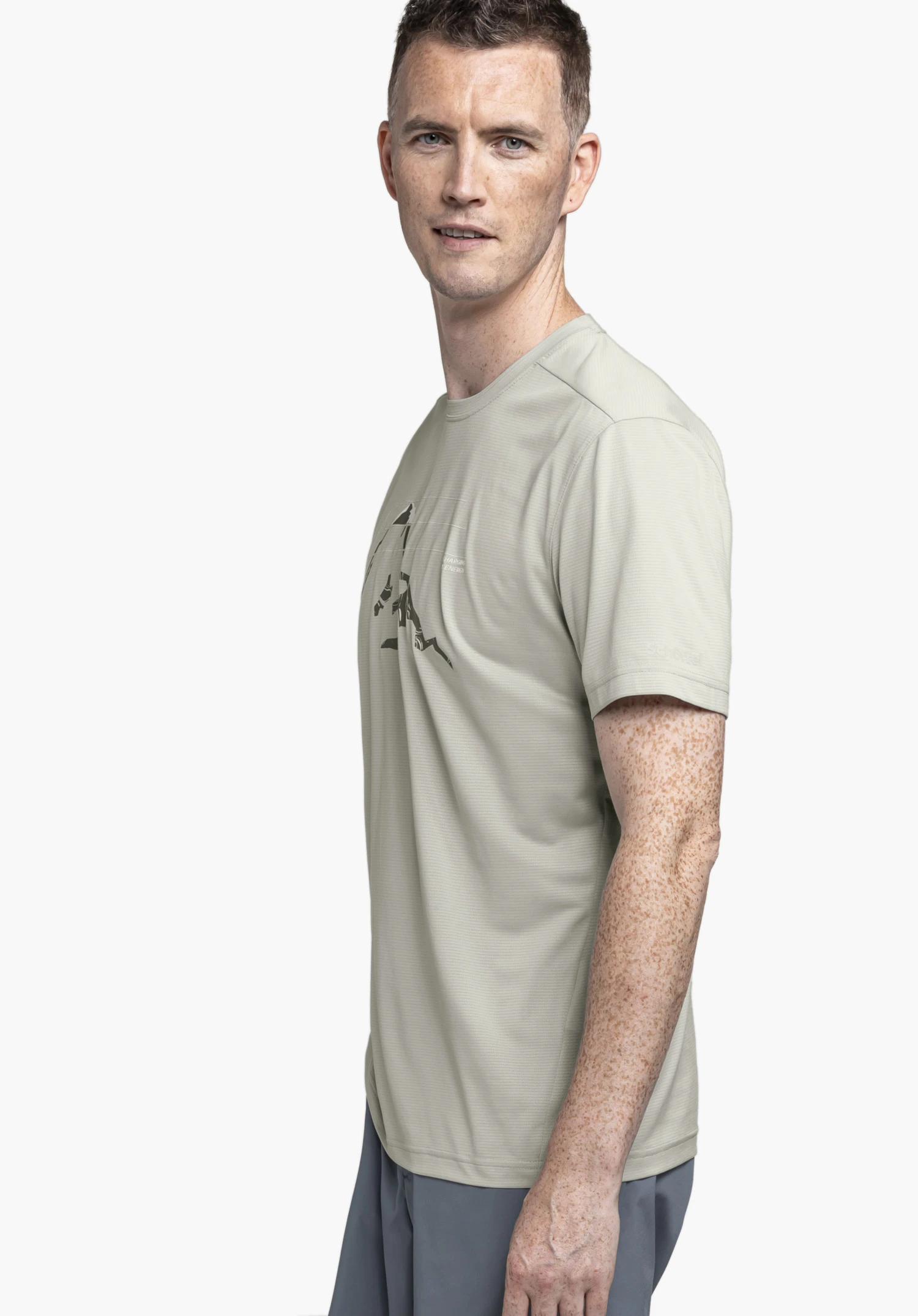 CIRC T Shirt Sulten M in Grau: Ein Model steht in Seitenansicht vor einem neutralen Hintergrund und trägt das T-Shirt mit einem markanten Grafikdruck auf der Brust. Das dezente Schöffel-Logo ist am Ärmel erkennbar.