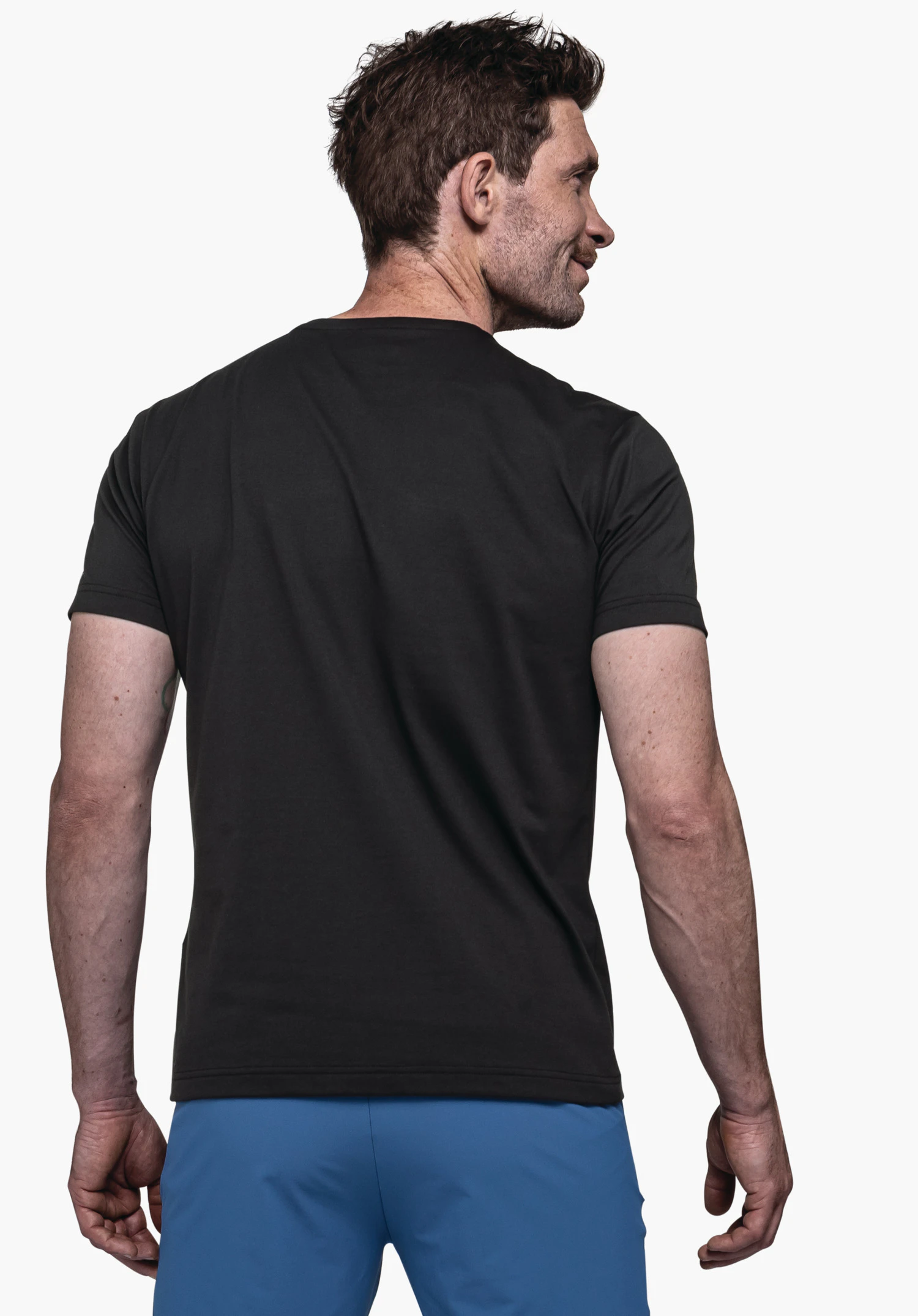 T Shirt Hohberg M in het zwart. Het model is te zien vanaf de achterkant en kijkt licht naar rechts, tegen een neutrale achtergrond.