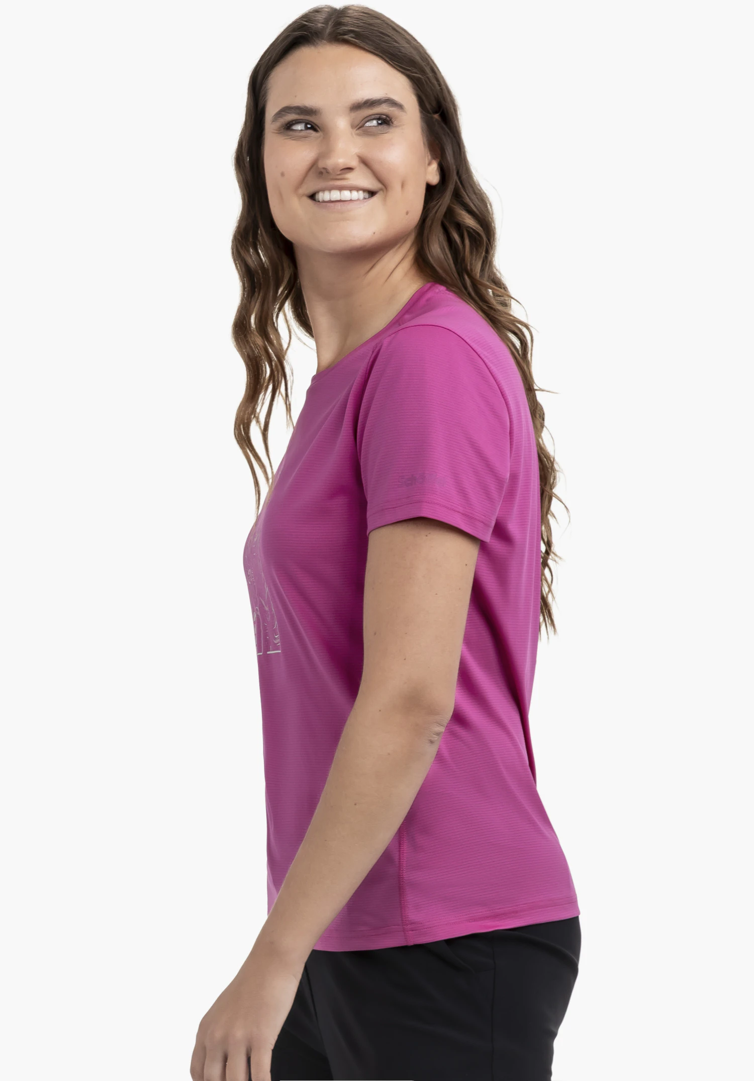 CIRC T Shirt Sulten L en rose : Une femme se tient de profil devant un fond neutre et sourit. Le t-shirt rose vif est mis en valeur par cette perspective latérale, laissant apparaître le logo Schöffel discret sur la manche.