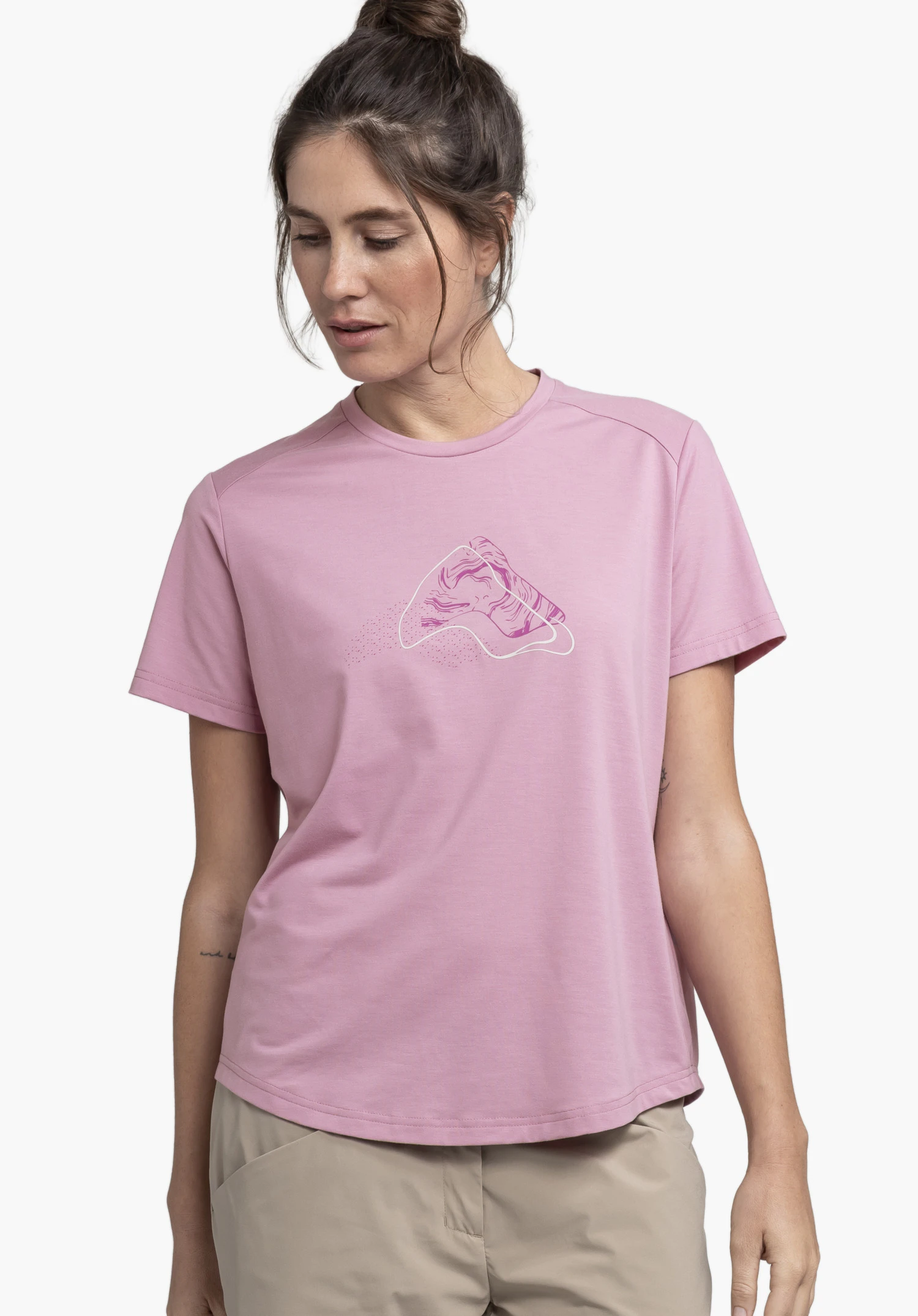 T Shirt Haberspitz L. Ein Model steht in der Frontalansicht, blickt leicht nach unten und präsentiert das rosafarbene Shirt mit einem grafischen Print auf der Brust vor einem neutralen Hintergrund.