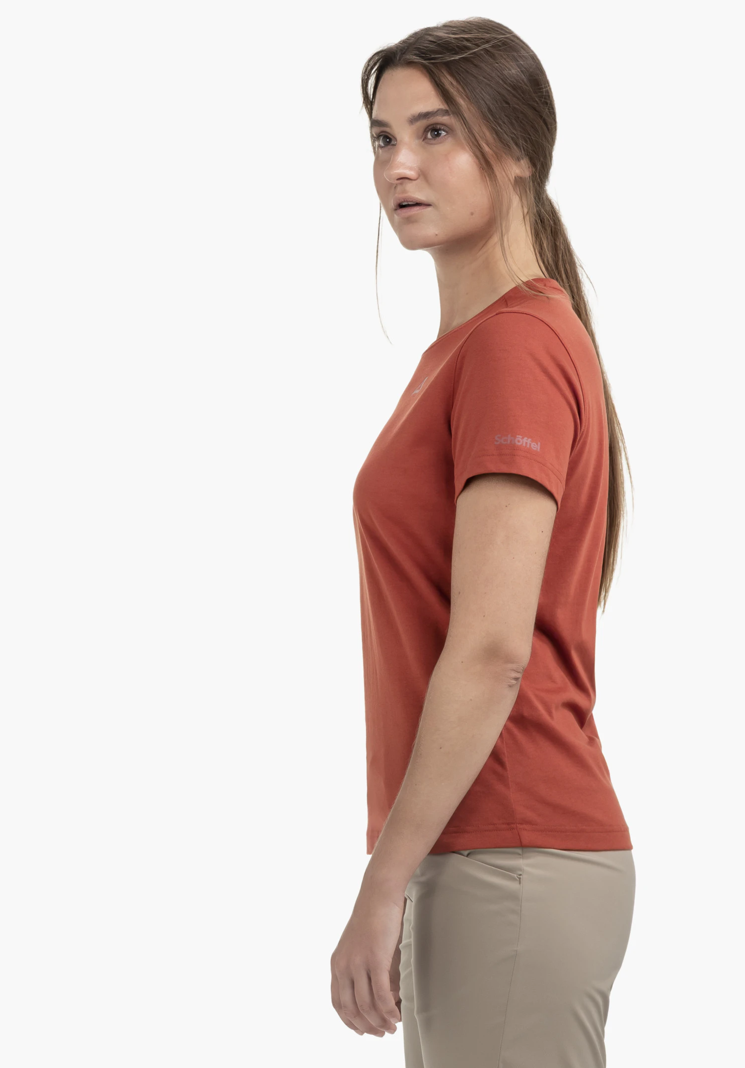 T Shirt Buchberg L in red. A woman stands sideways in front of a neutral background, wearing the shirt which clearly shows the subtle Schöffel logo on the sleeve.