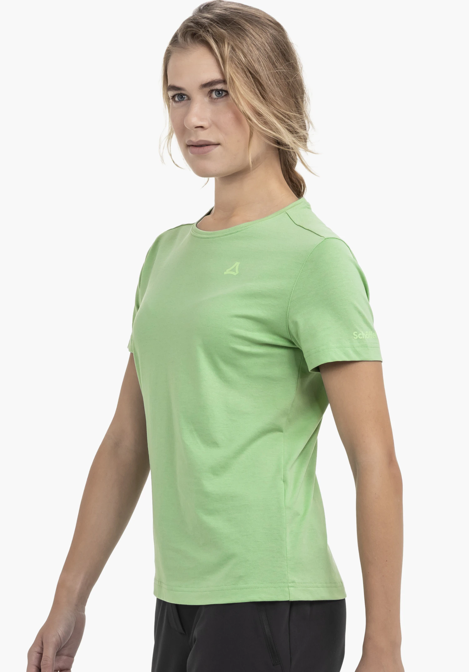 T Shirt Buchberg L in green captured against a neutral background: The model stands in a side-profile pose, showcasing the shirt, which features subtle Schöffel branding on the chest and sleeve.