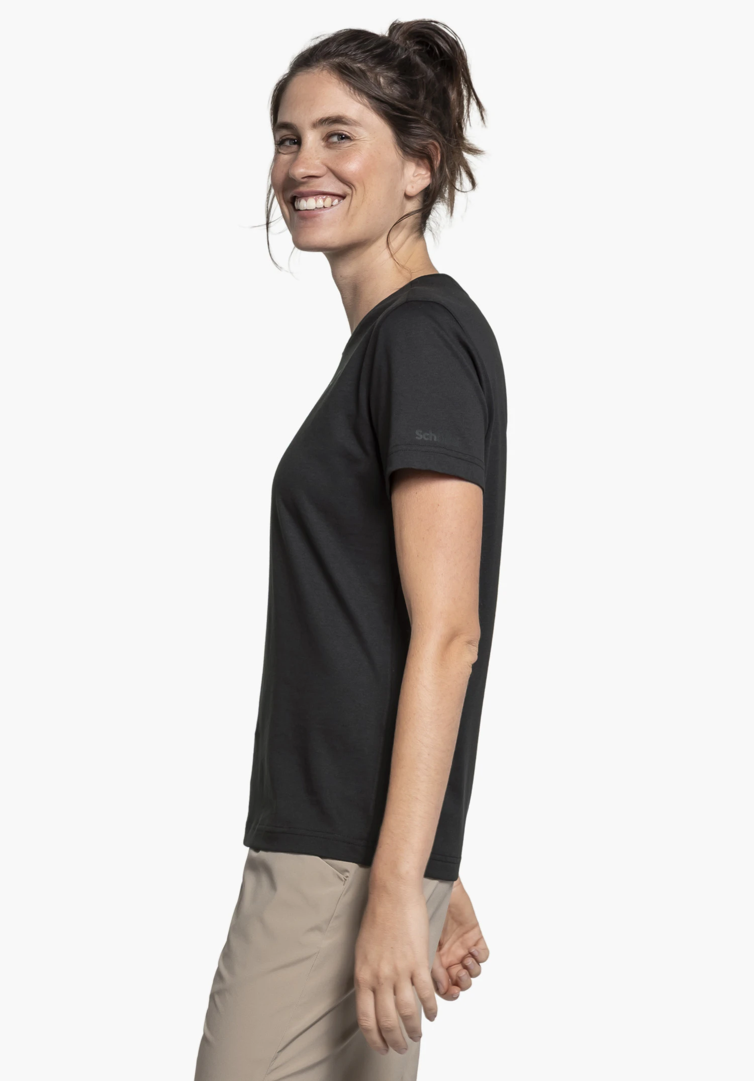 T Shirt Buchberg L in black: A smiling woman stands sideways against a neutral background, showcasing the T-shirt. The subtle Schöffel logo on the sleeve is clearly visible.