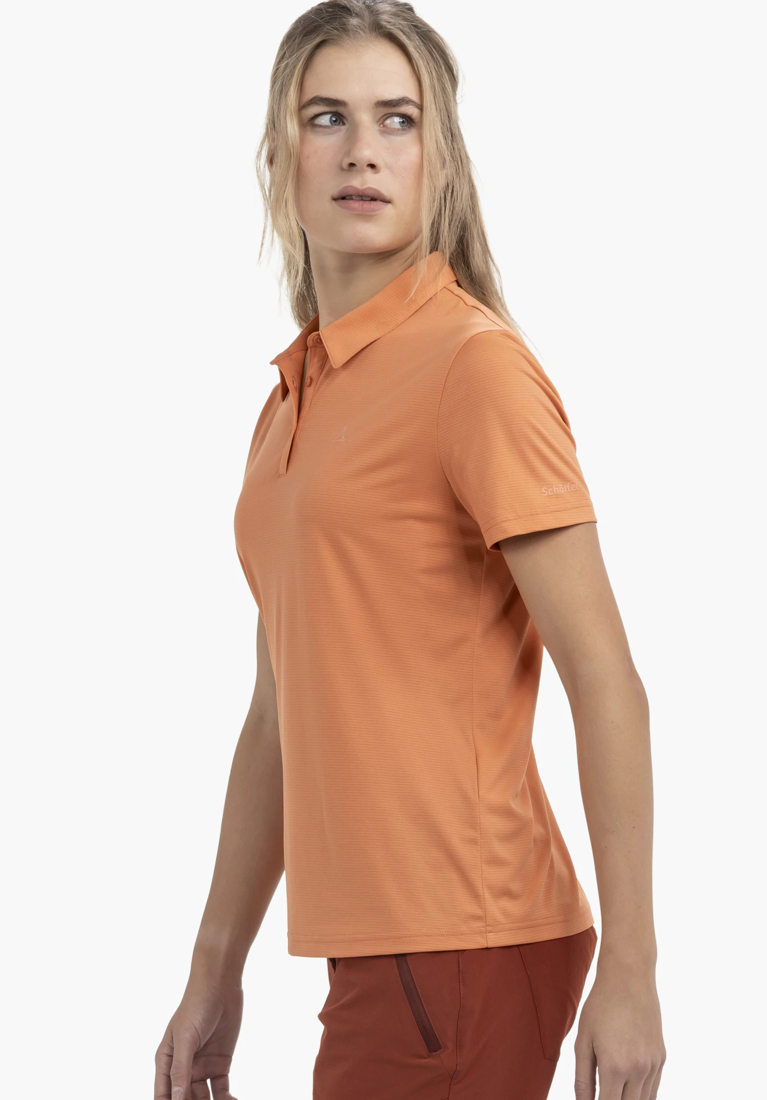 CIRC Polo Shirt Tauron L en orange vif. Le mannequin pose de profil devant un fond neutre, le regard tourné vers l'épaule, mettant ainsi en valeur le logo Schöffel discret sur la manche.