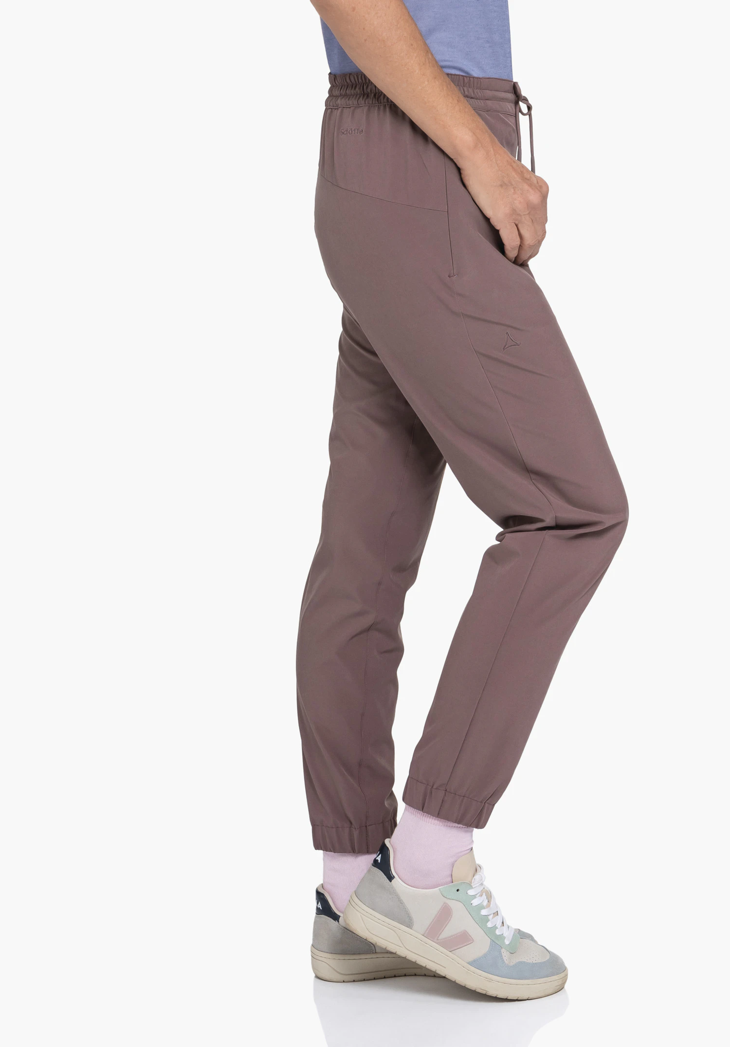 Pants Vienna L in Braun: Eine Person steht seitlich vor einem neutralen Hintergrund und präsentiert die Hose. Das dezent platzierte Schöffel-Logo am Oberschenkel unterstreicht den hochwertigen Look.