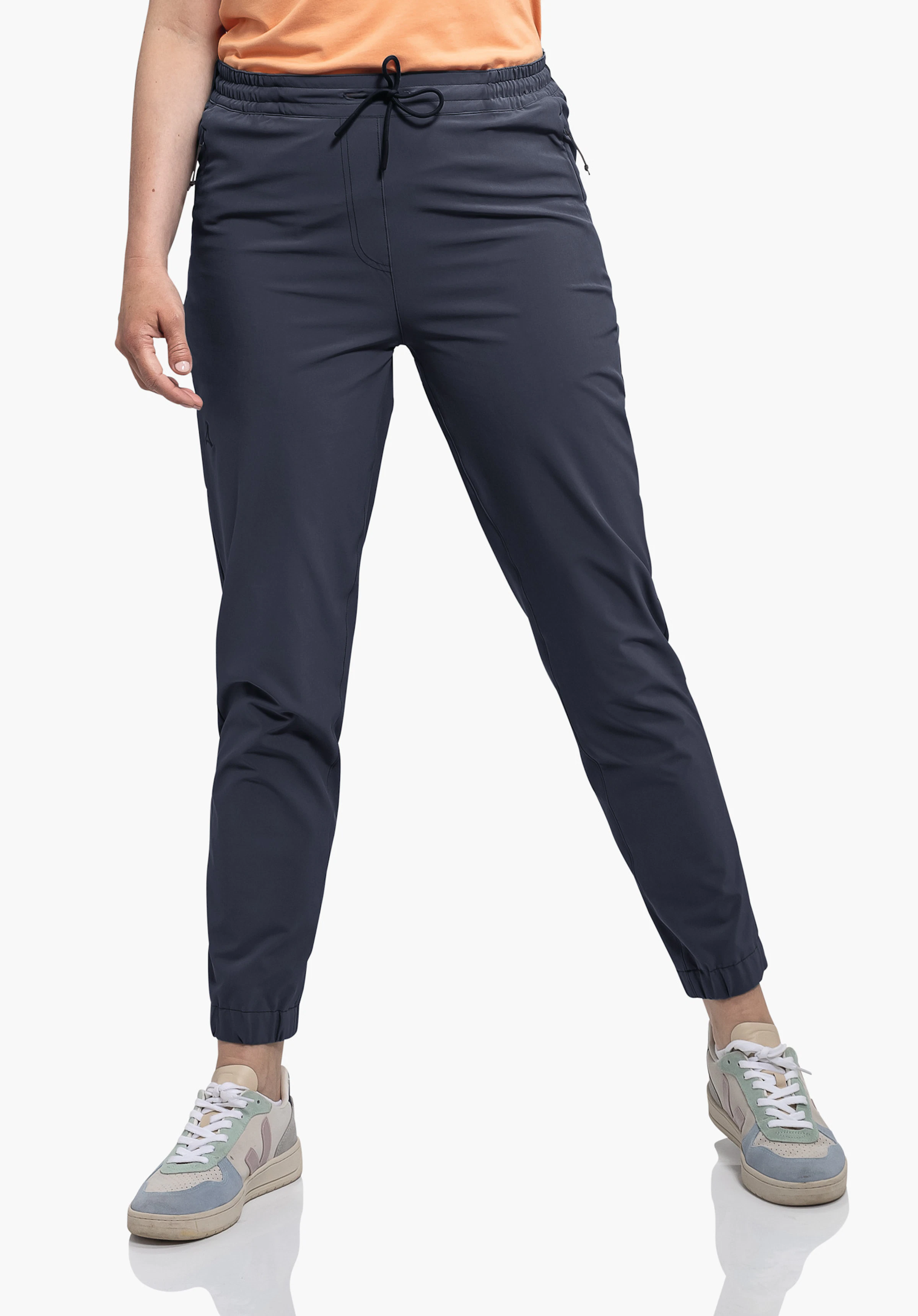 Pants Vienna L in Blau, getragen von einem Model, das frontal mit leicht gegrätschten Beinen steht. Das Schöffel-Logo ist am rechten Oberschenkel erkennbar, abgebildet vor einem neutralen Hintergrund.