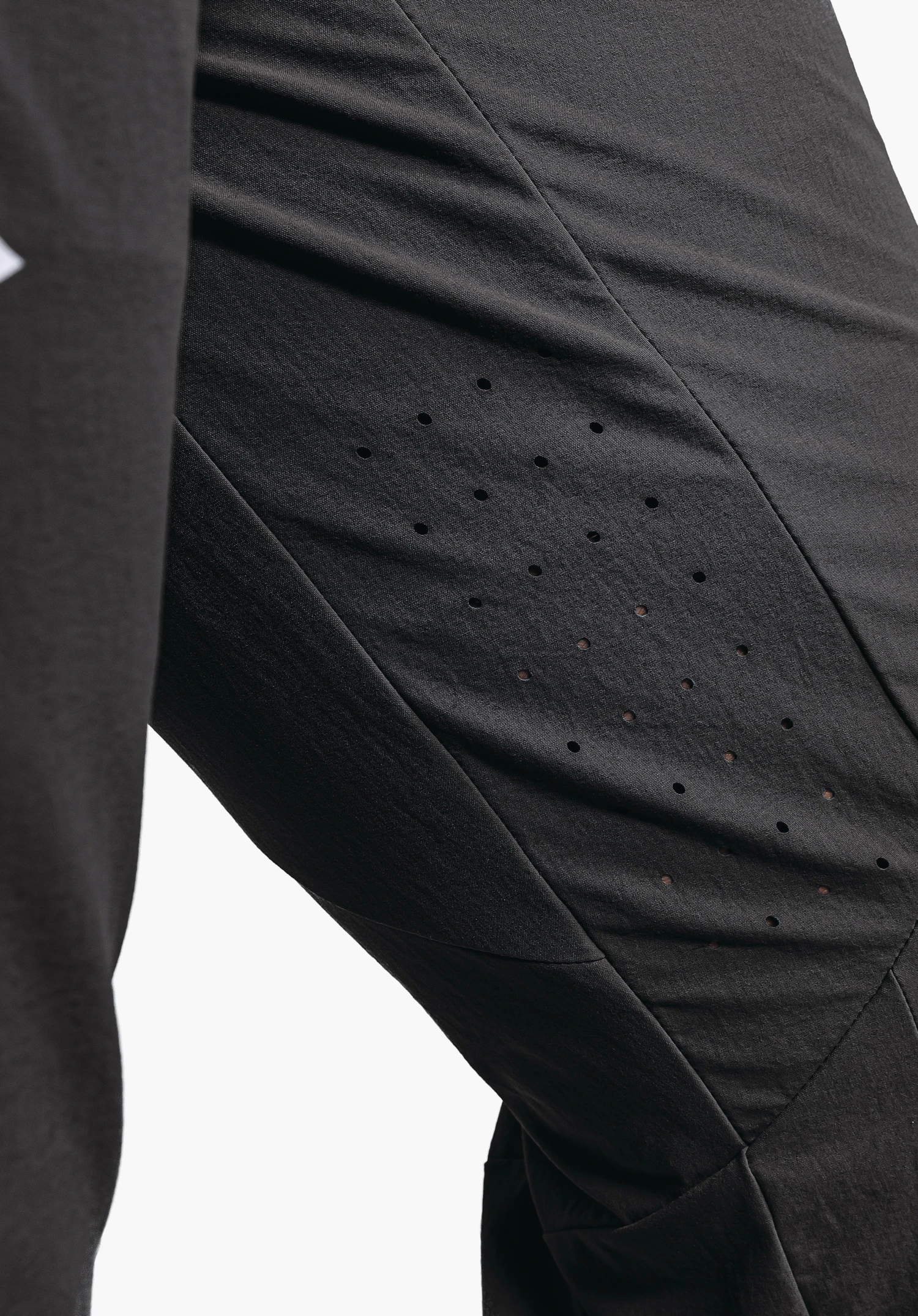 Pants Arosa M montre les perforations d'aération découpées au laser à l'intérieur de la cuisse et une partie du logo Schöffel blanc sur le tissu noir, gros plan sur fond blanc/neutre.