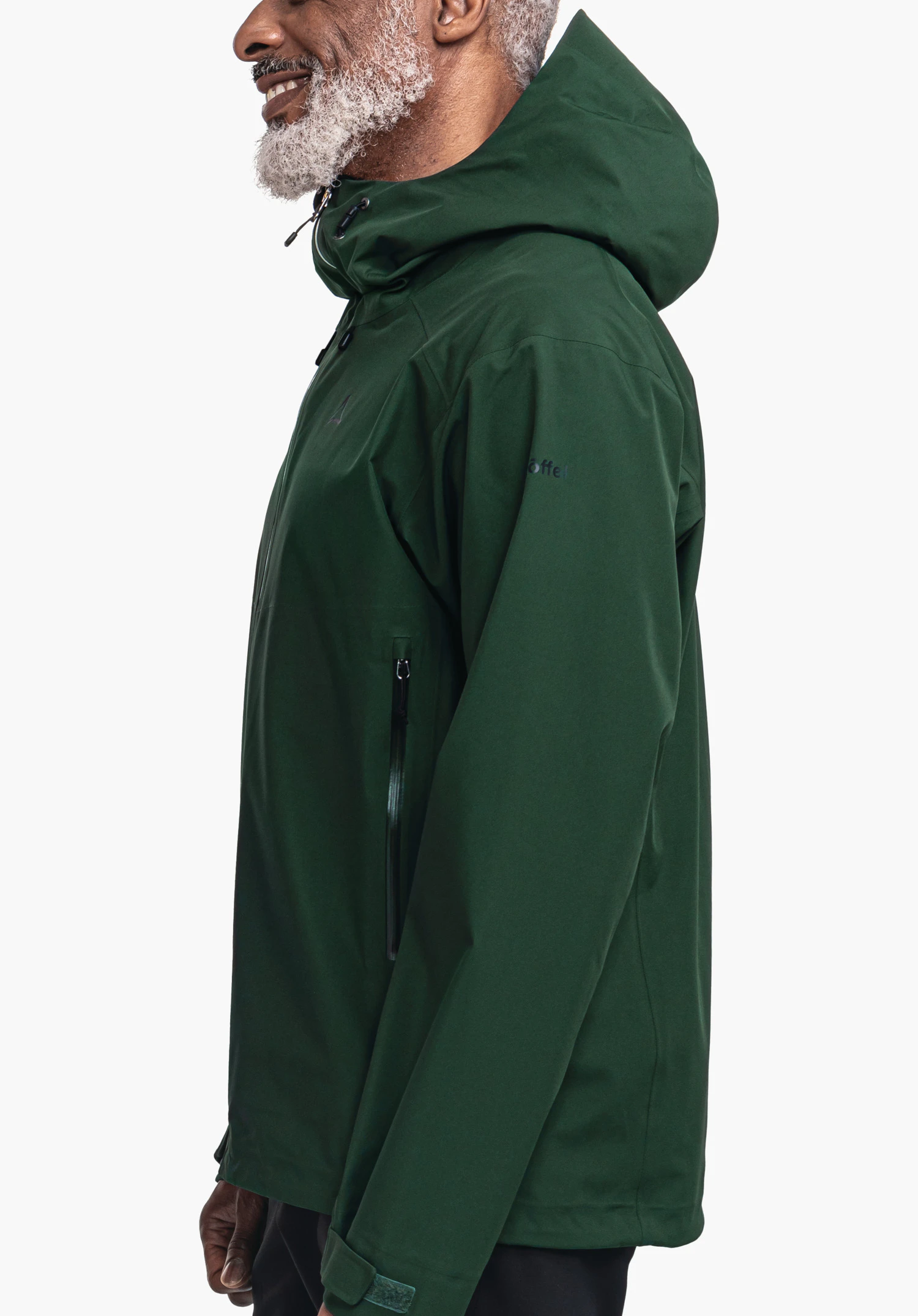Jacket Style Cascata MNS donkergroene regenjas, gedragen door een glimlachende man in profiel; lichtgrijze baard zichtbaar; staande studio-opname voor een witte achtergrond.
