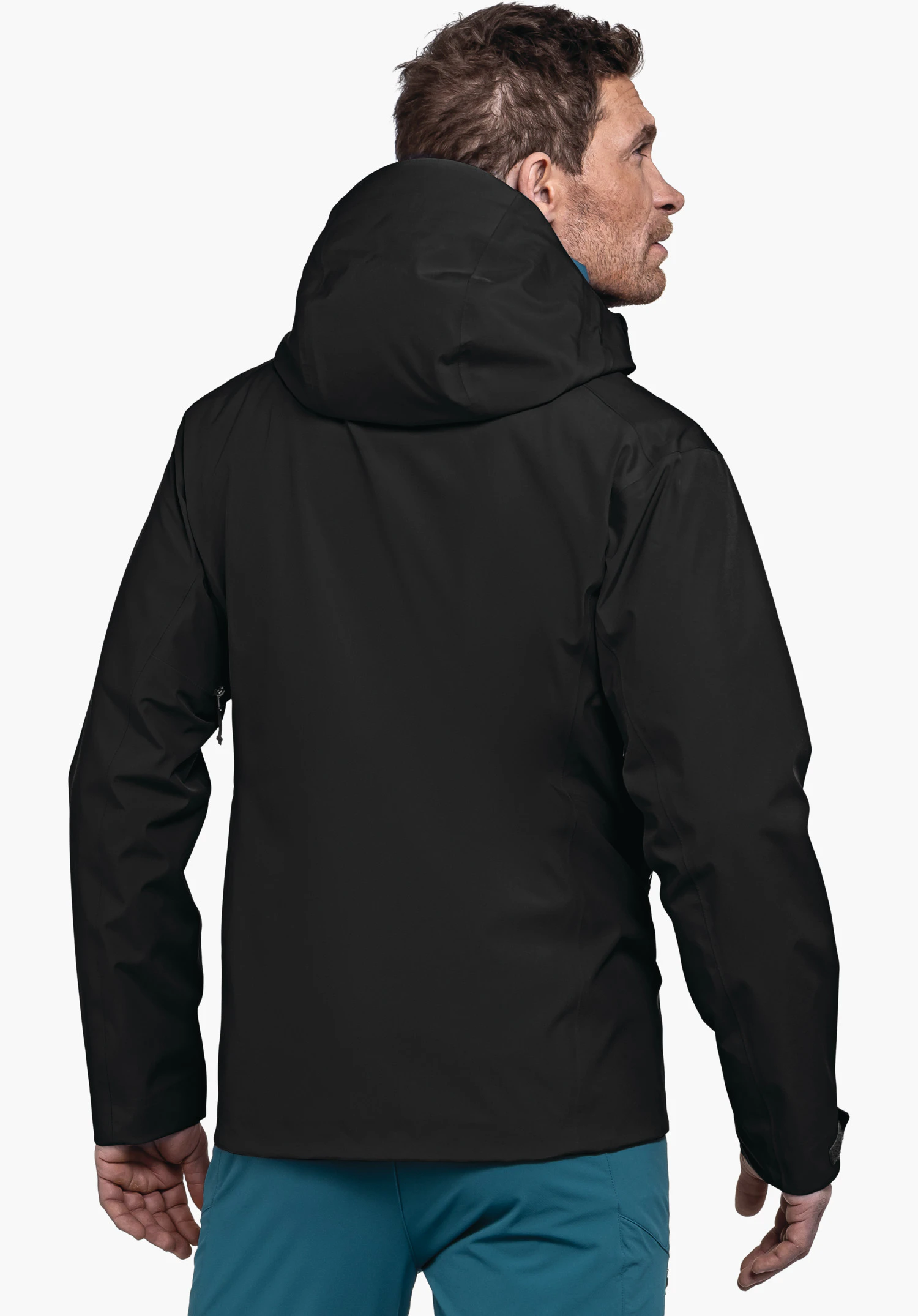 Jacket Style Cascata MNS veste noire avec capuche; un homme la porte, se tient dos à la caméra et regarde légèrement vers la droite; pantalon bleu clair; fond blanc.