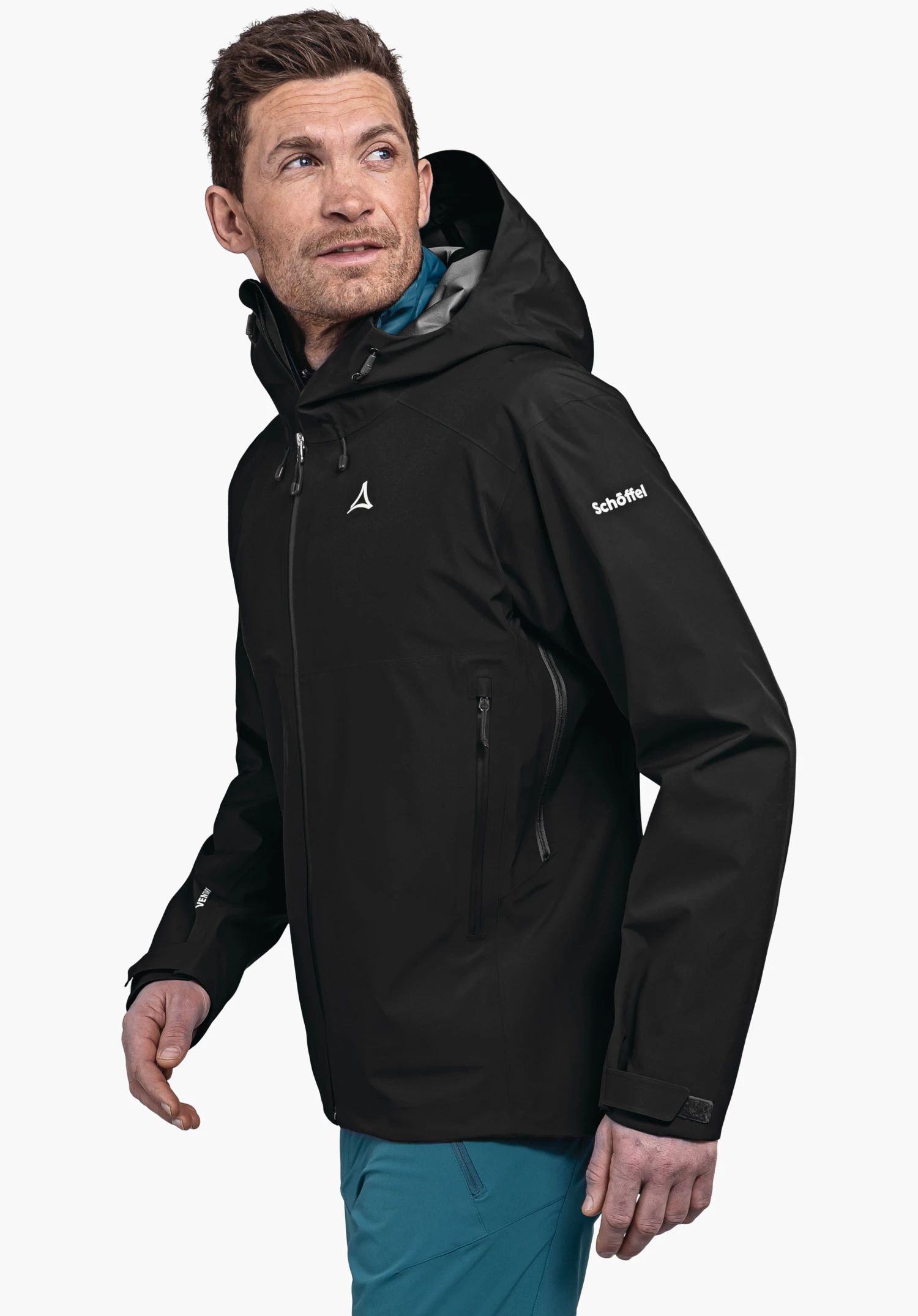 Jacket Style Cascata MNS veste noire à capuche avec logo Schöffel; homme la porte et regarde vers le haut à droite, doublure intérieure bleu clair, pantalon bleu, fond neutre; texte: "Schöffel".