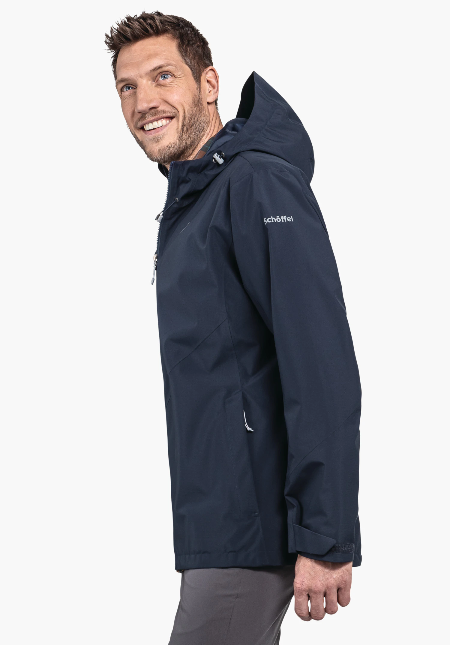 Jacket Style Yew MNS veste extérieure bleu foncé portée par un homme souriant en profil, capuche relevée, bras le long du corps, devant un fond blanc. Texte: "schöffel".