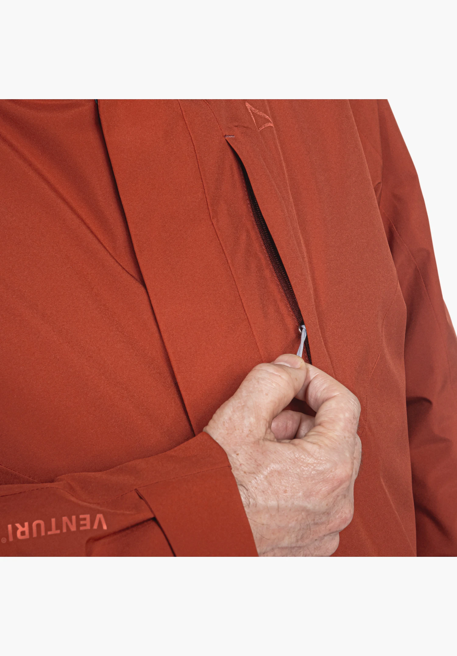 3in1 Jacket Style Tamina MNS zeigt die rote Brusttasche mit Reißverschluss, der von einer Hand bedient wird, sowie den VENTURI-Schriftzug am Ärmel und das gestickte Schöffel-Logo. Nahaufnahme vor weißem/neutralem Hintergrund.