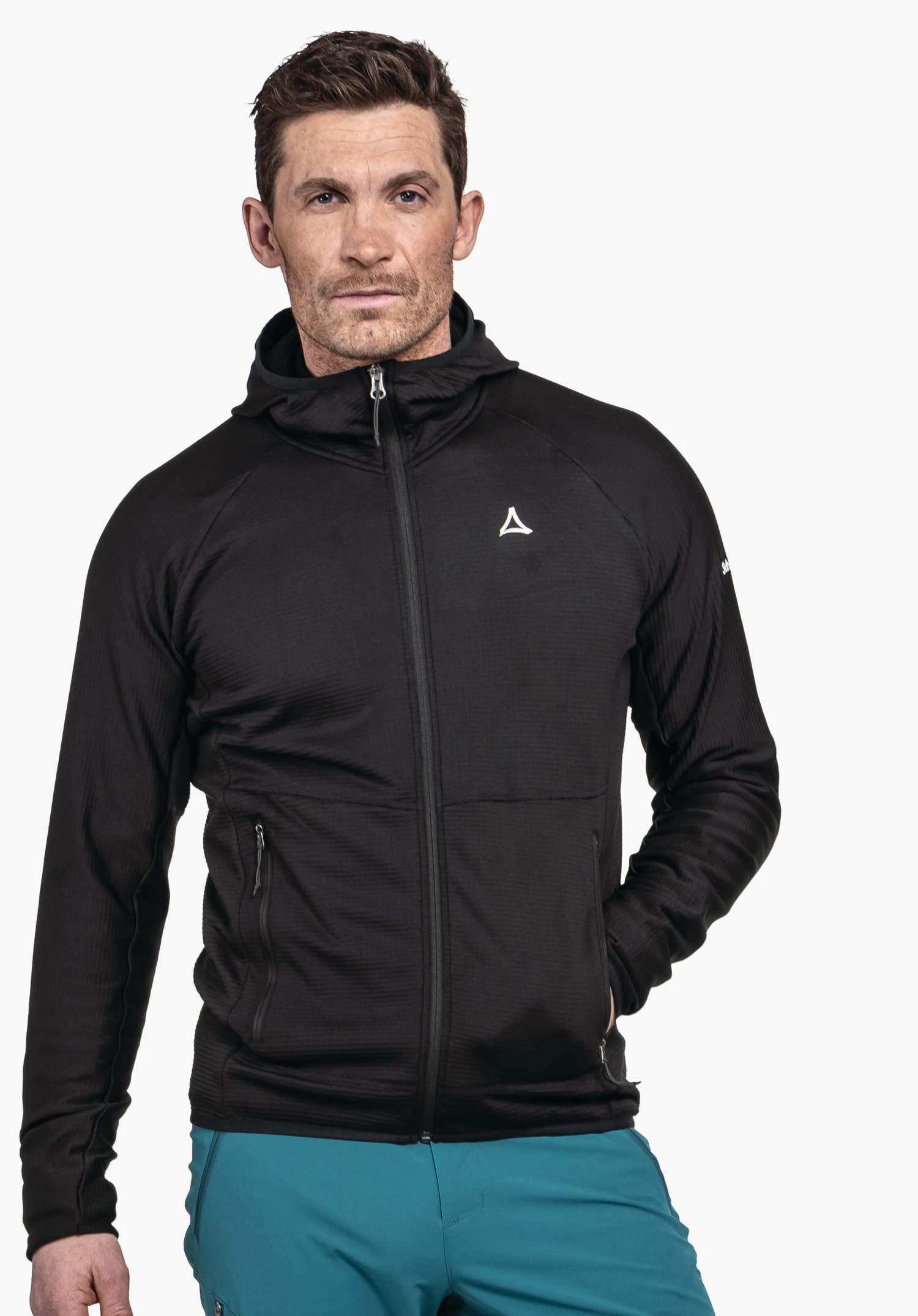 Fleece Hoody Style Cascata MNS. Ein Model steht frontal mit einer Hand in der Seitentasche und trägt den Hoody in schwarz mit deutlich sichtbarem Schöffel-Logo auf der linken Brust. Das Bild ist vor einem neutralen Hintergrund aufgenommen.
