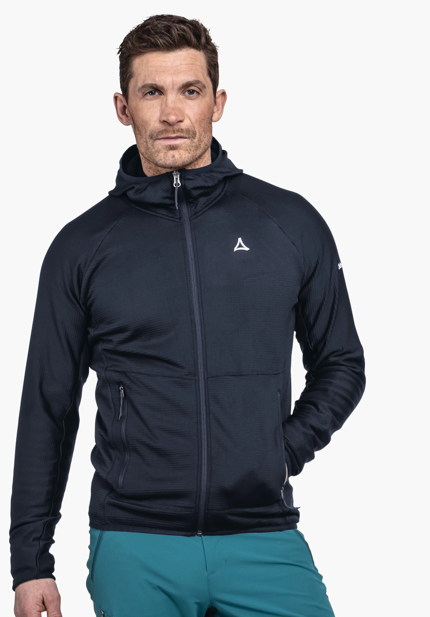 Fleece Hoody Style Cascata MNS. Un mannequin homme porte le sweat à capuche bleu et se tient de face avec une main dans la poche latérale. Le Schöffel-Logo est bien visible sur la poitrine gauche. L'image est présentée sur un fond neutre.