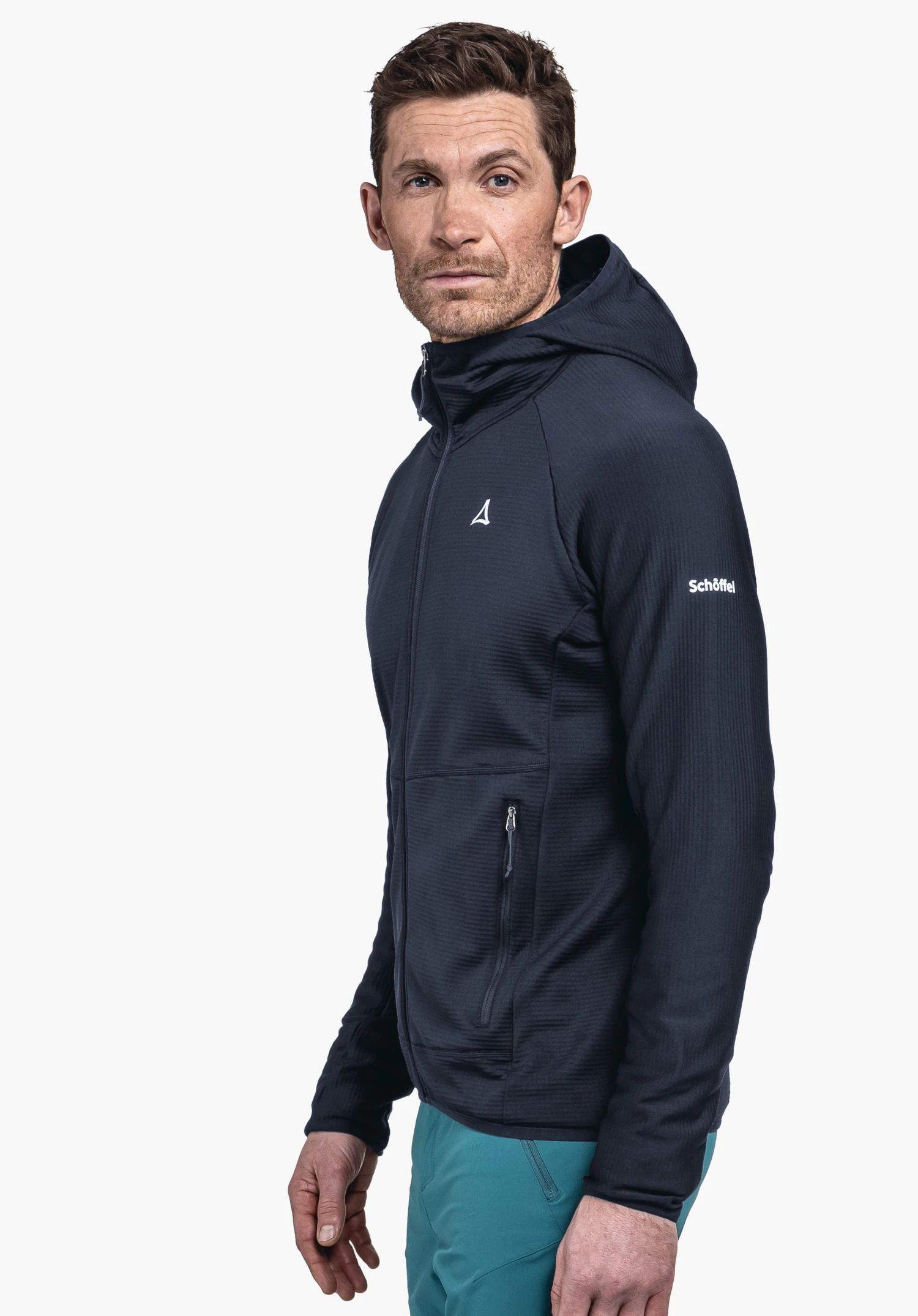 Fleece Hoody Style Cascata MNS en bleu. Un modèle masculin est présenté de profil devant un fond neutre, portant le sweat à capuche en polaire. Le logo Schöffel discret sur le haut du bras est bien visible.