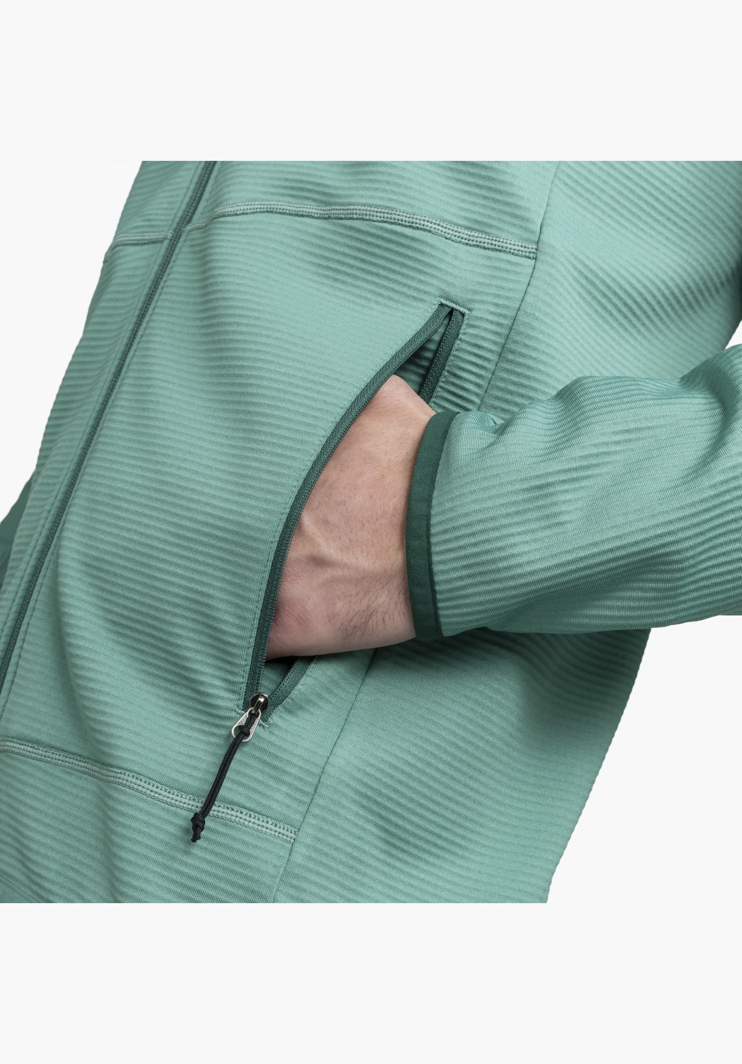 Fleece Jk Style Cascata MNS en vert, montrant une main dans la poche zippée ouverte avec un tire-zip noir, la texture côtelée du tissu polaire et la bordure vert foncé du poignet, gros plan sur fond blanc/neutre.