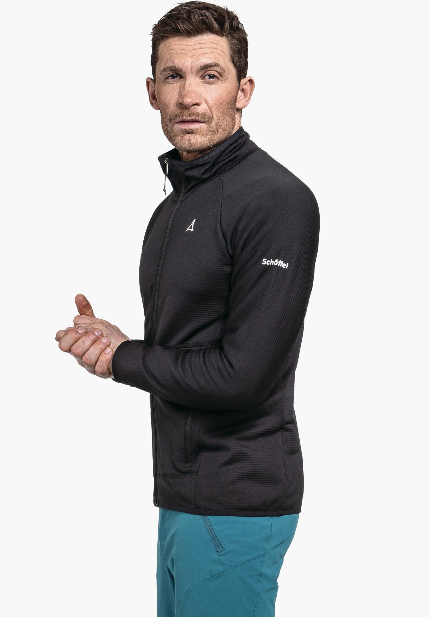 Fleece Jk Style Cascata MNS Mann trägt schwarze Jacke mit Schöffel-Logo, hält die Hände zusammen und blickt seitlich, vor hellweißem Hintergrund. Schriftzug: Schöffel.